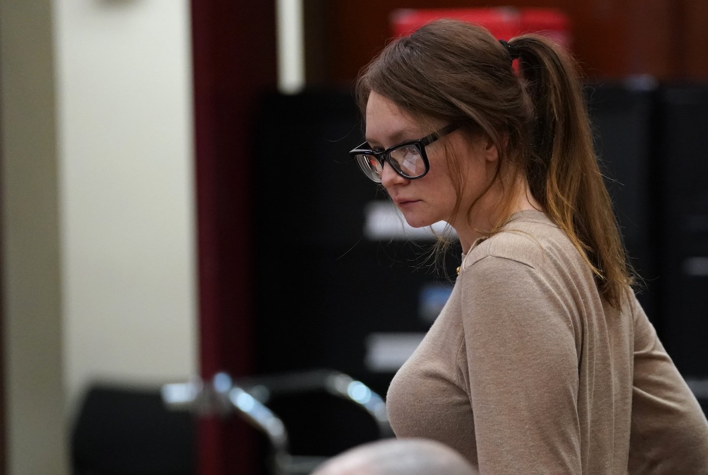 Anna Delvey, known as Anna Sorokin wears glasses and looks down while in court 
