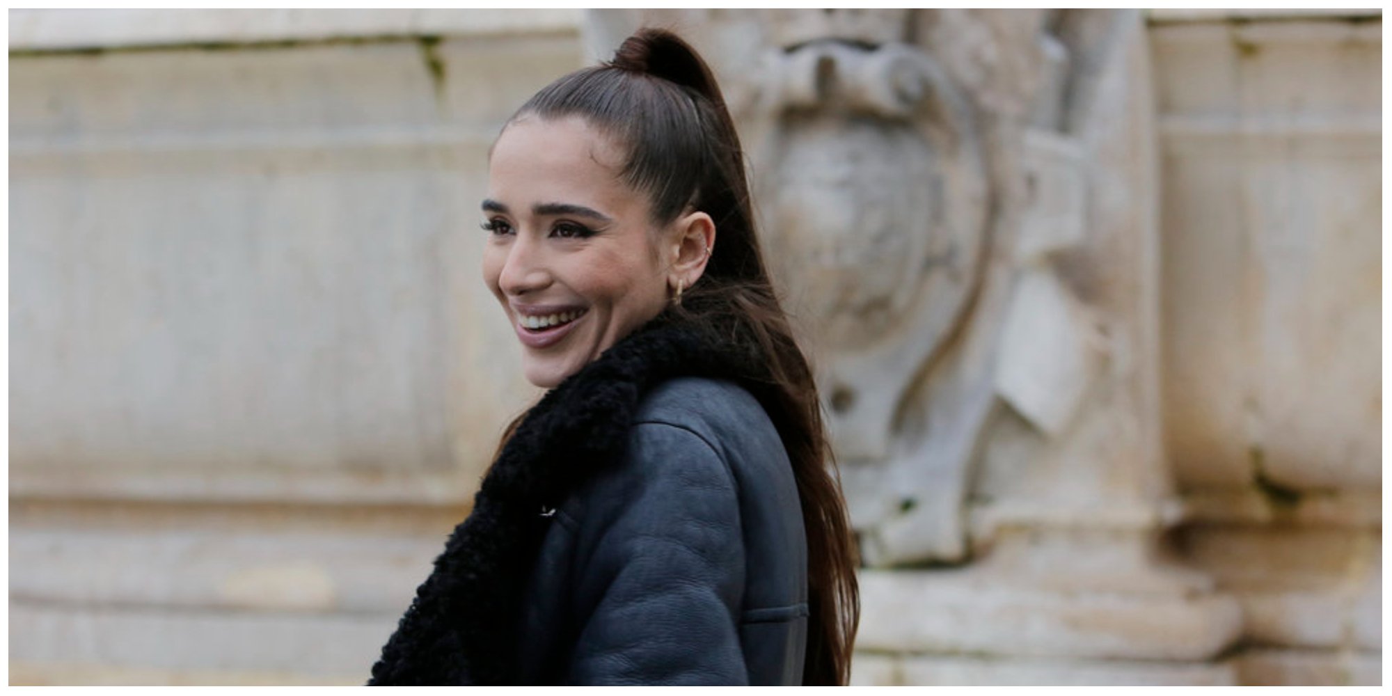 Margaux Lignel from 'Real Girlfriends in Paris' smiles while wearing a black jacket and hair in a ponytail
