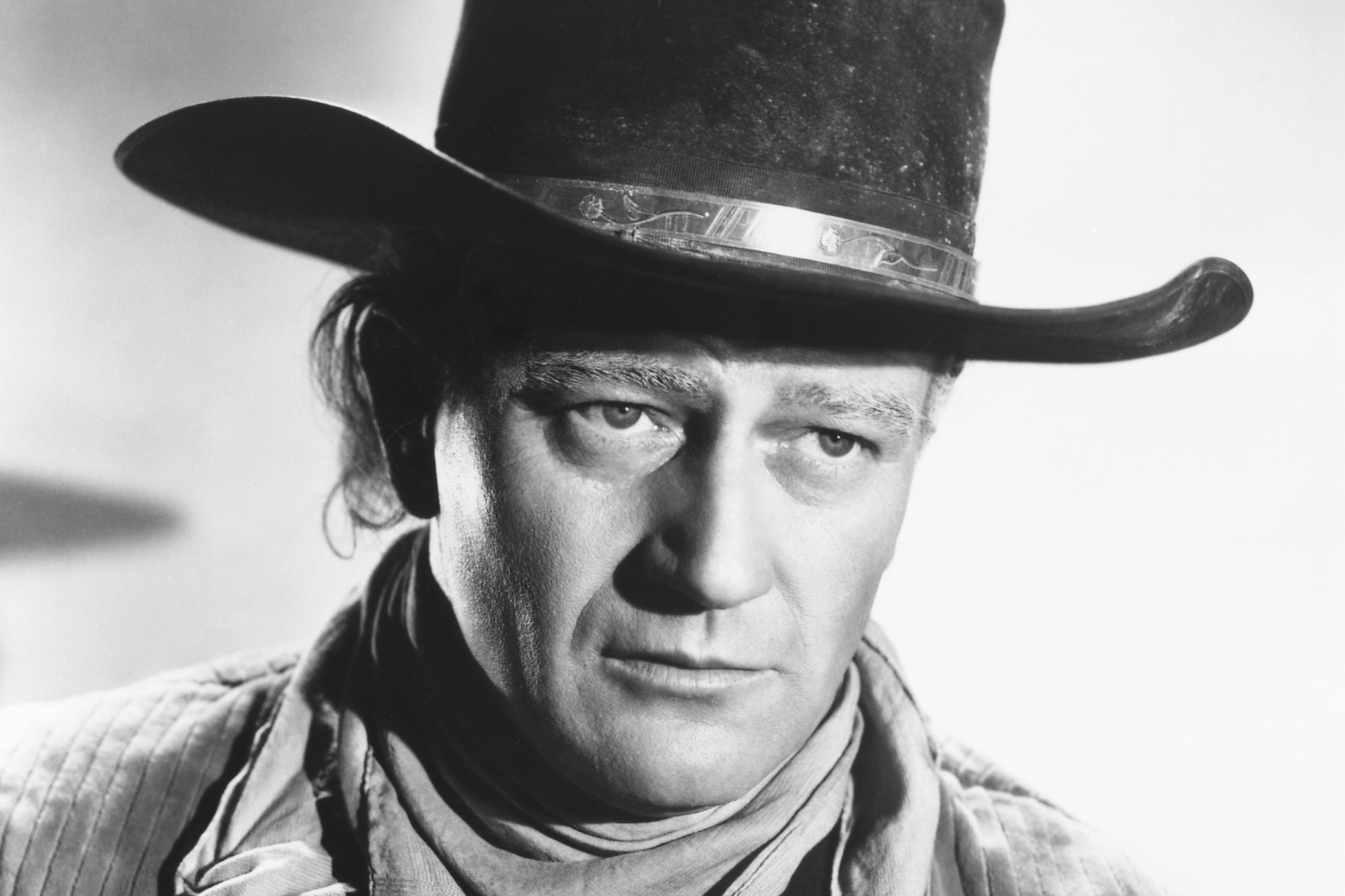 'Red River' John Wayne wearing a cowboy hat and a white neckerchief, in a studio portrait.