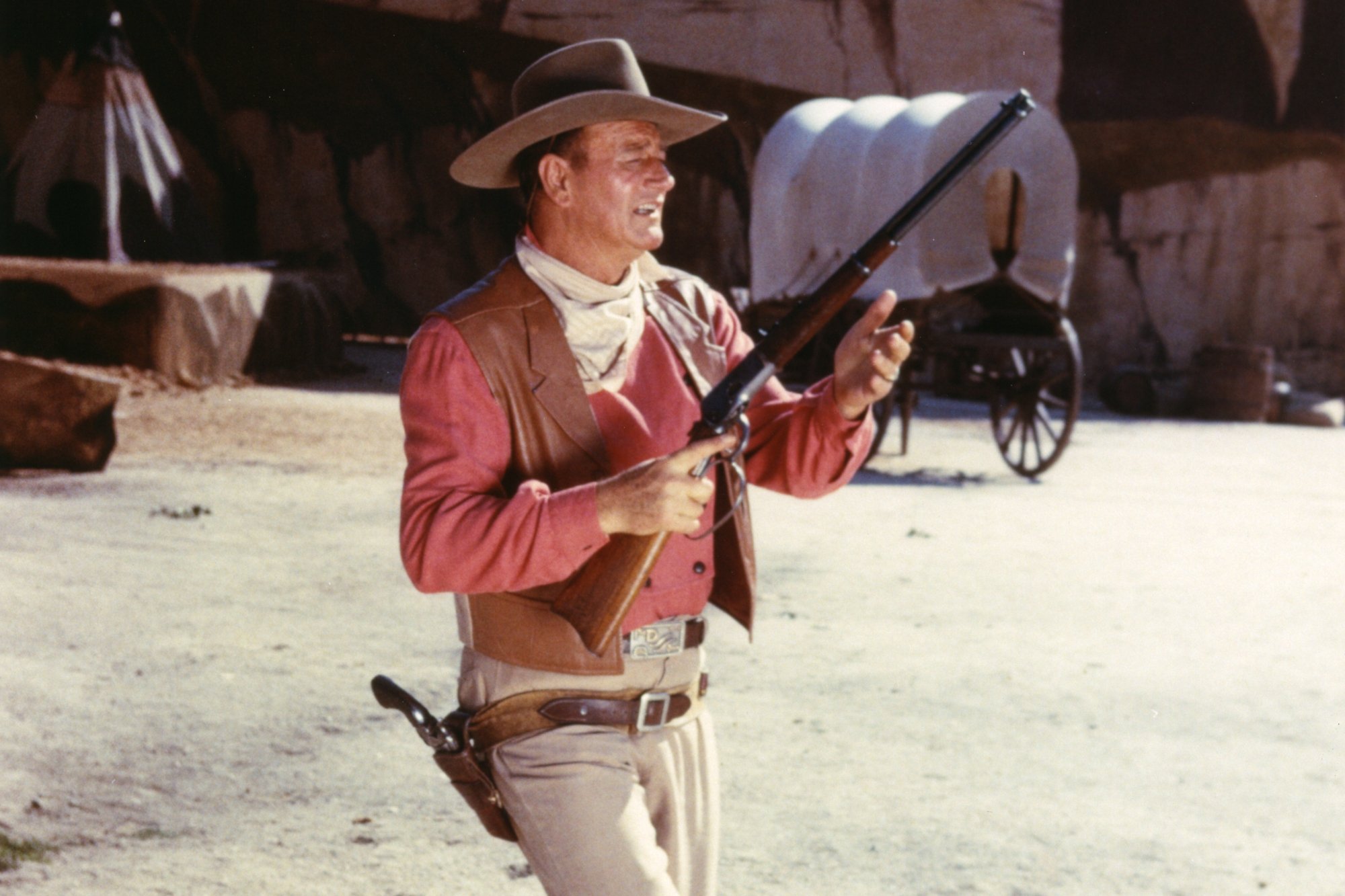 'Rio Bravo' John Wayne wearing a cowboy uniform carrying a gun with a wagon in the background