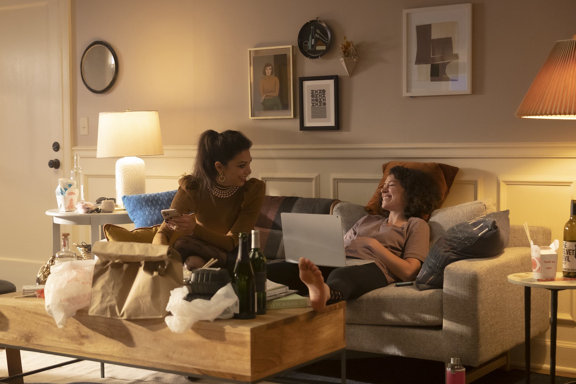 Ginger Gonzaga and Tatiana Maslany, in character as Nikki Ramos and Jennifer Walters in 'She-Hulk: Attorney at Law' on Disney+, which may feature the introduction of the Fantastic Four, share a scene on the couch. Nikki wears a brown long-sleeved shirt and tights. Jennifer wears a gray shirt and black leggings.