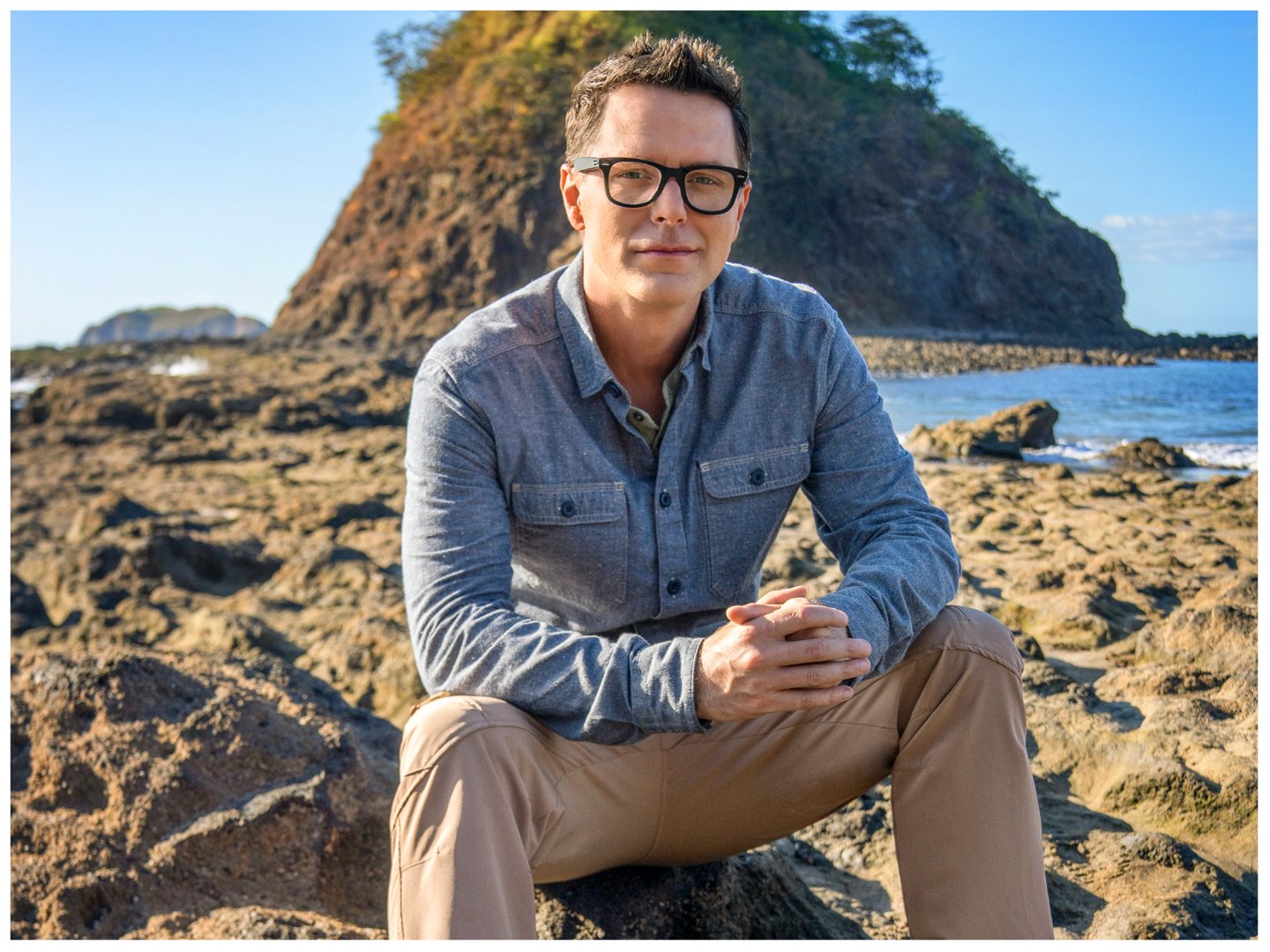 Bobby Bones from 'Snake in the Grass' sits on a rock with hands folded