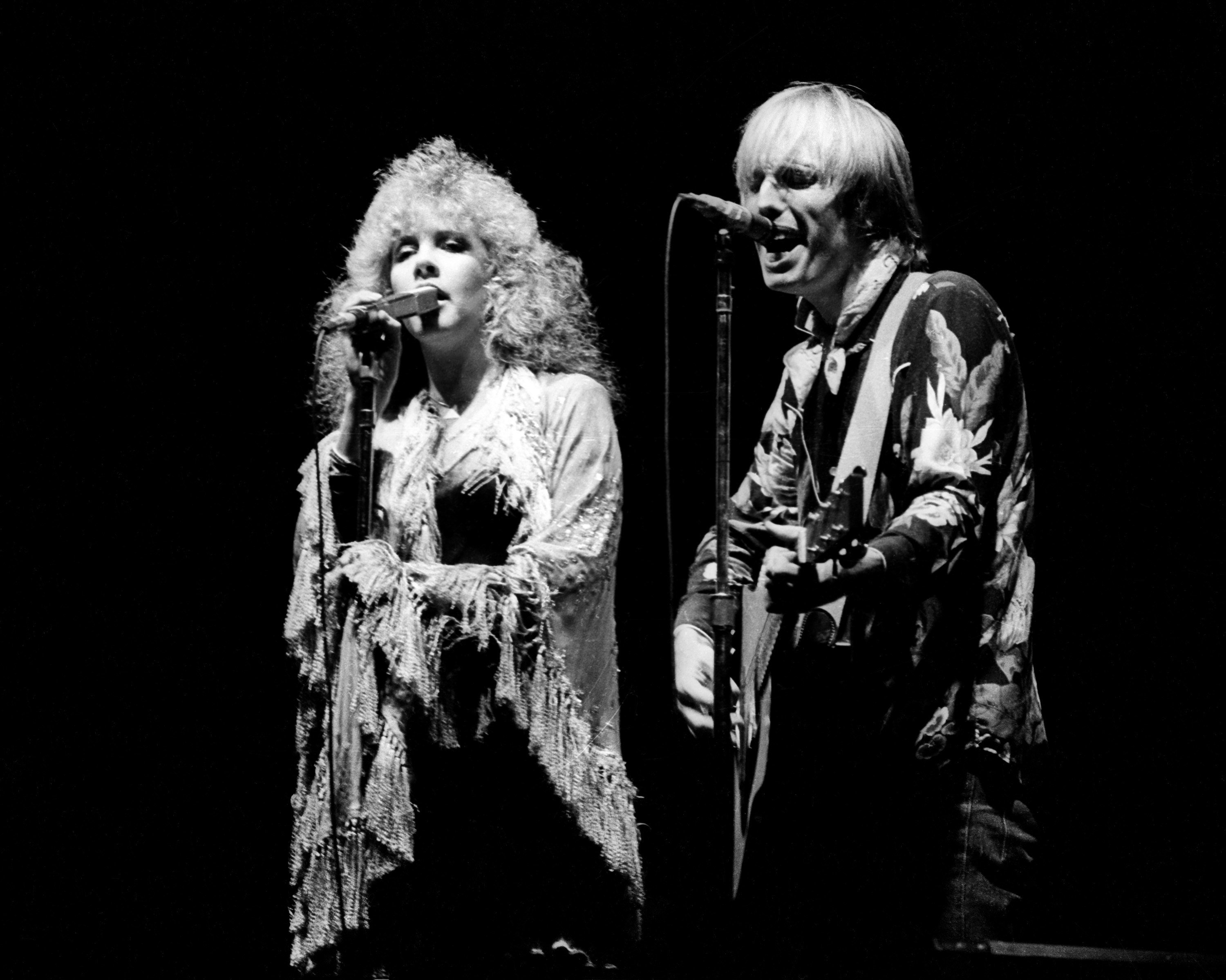 A black and white picture of Stevie Nicks and Bob Dylan singing into microphones. 