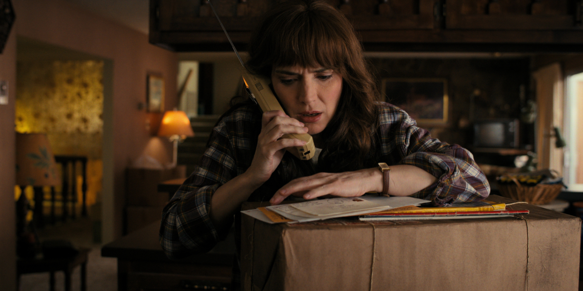 Joyce Byers talks on the phone and looks at her mail in Stranger Things Season 4. 