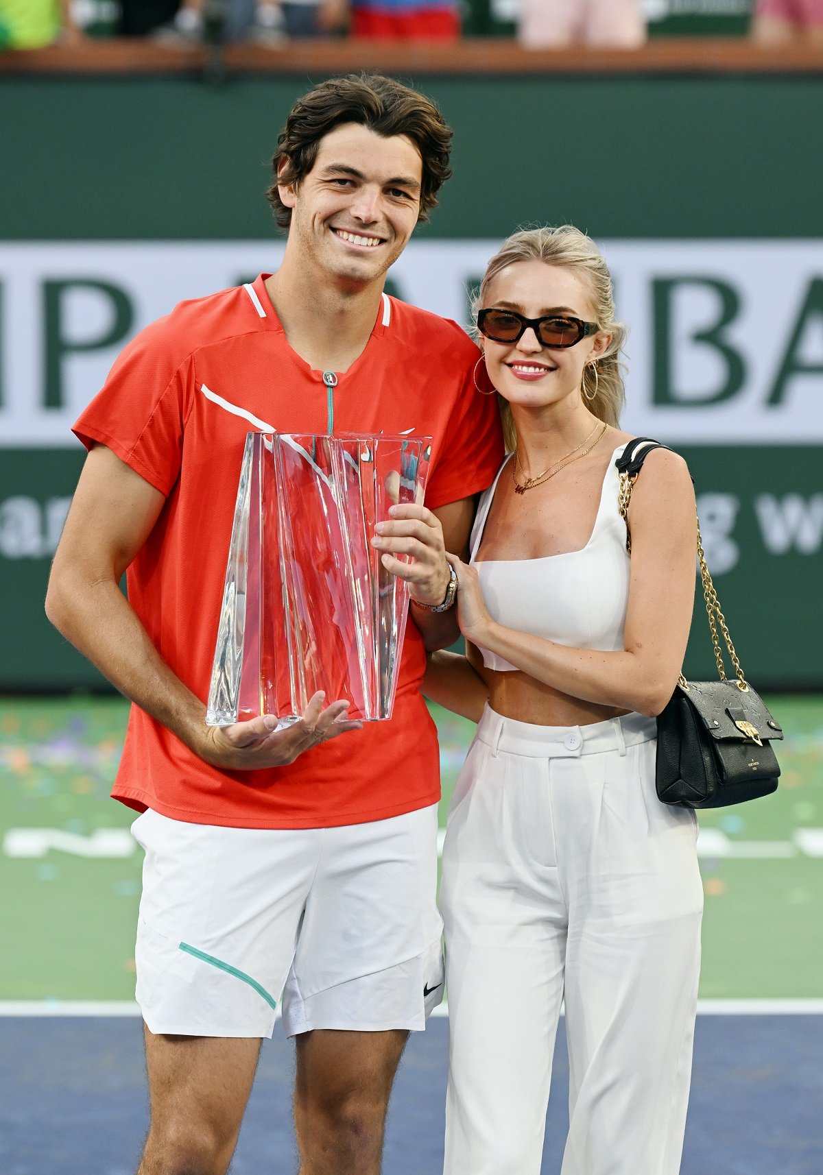 Taylor Fritz posing on the court with girlfriend Morgan Riddle after winning a finals tennis match at the BNP Paribas Open