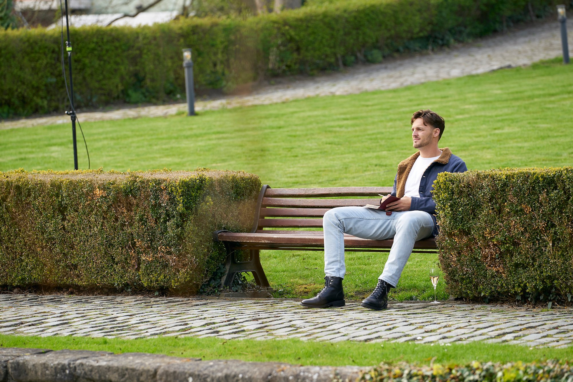 The Bachelorette contestant Logan caught COVID-19 and left the season early. Logan's seen here sitting on a bench outside.