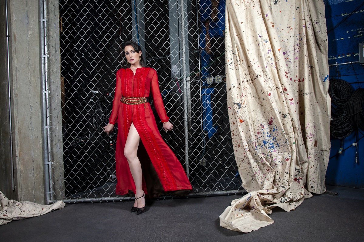 'The Bold and the Beautiful' star Rena Sofer wearing a red dress and posing in front of a chain link fence.