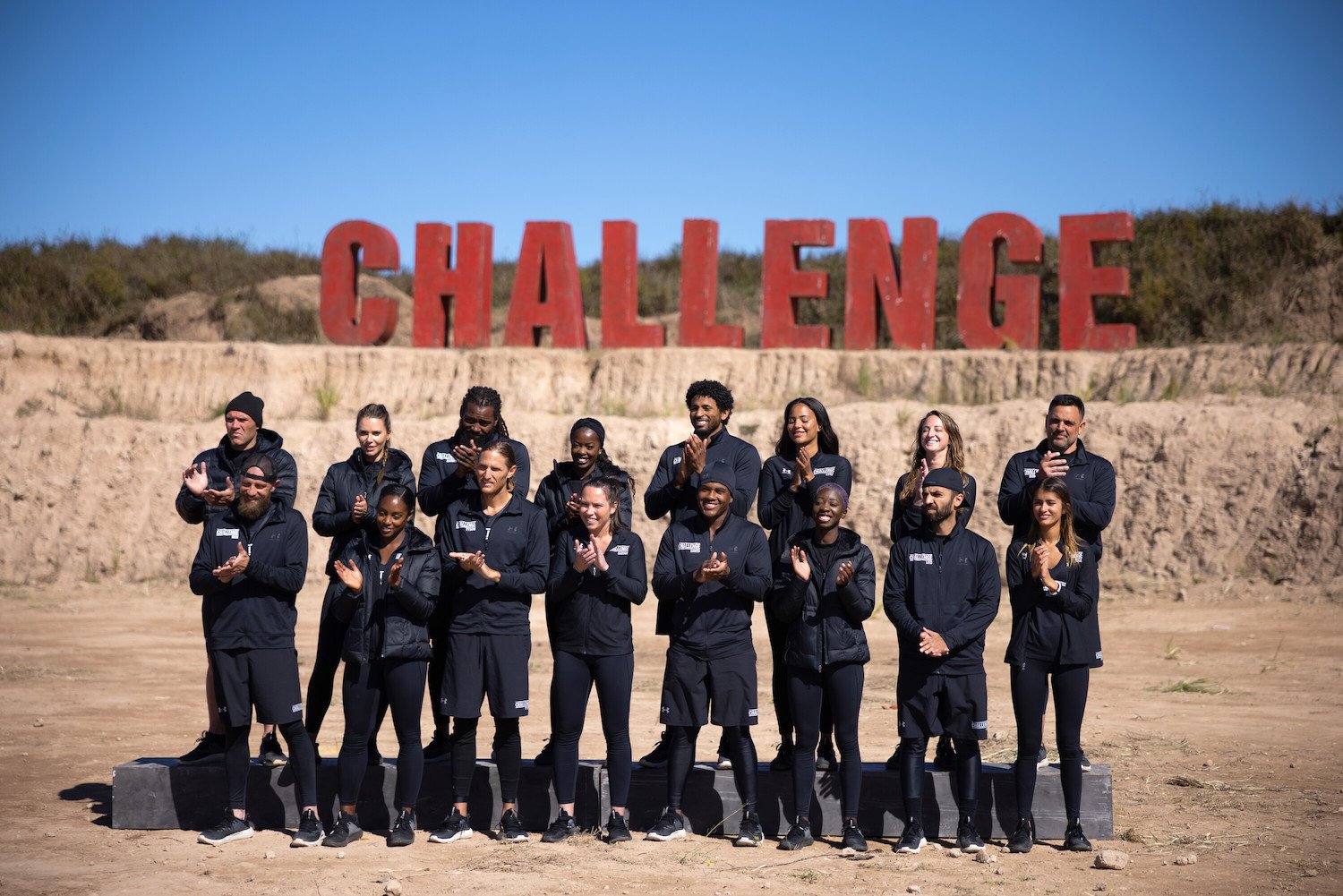 The cast of 'The Challenge: USA' episode 7 standing together in the desert in front of a 'Challenge' sign