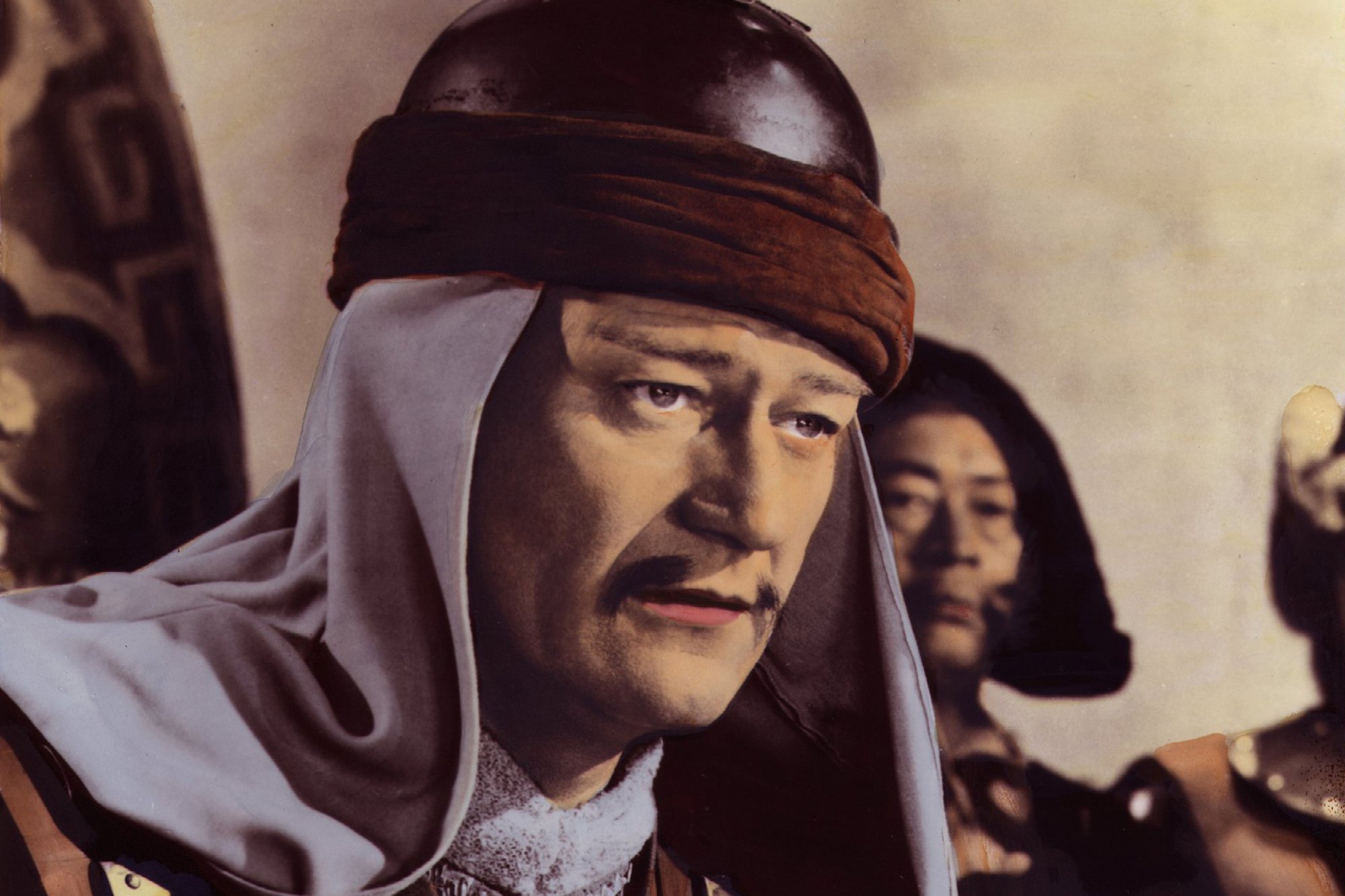 'The Conqueror' John Wayne as Genghis Khan wearing a mustace, hate, and hooded clothing