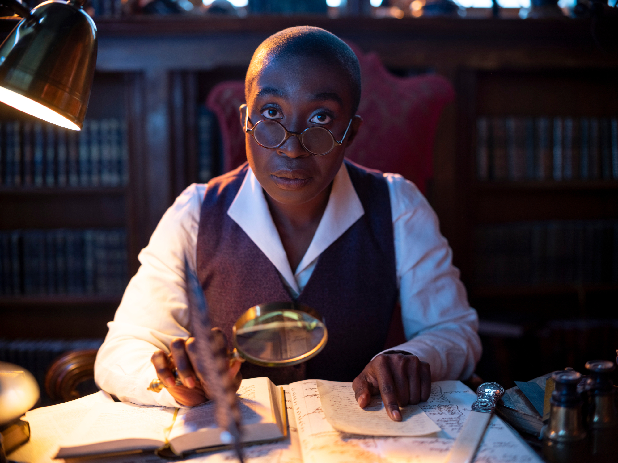 Vivienne Acheampong as Lucien in the cast of 'The Sandman.' She's sitting at a desk with papers in front of her.
