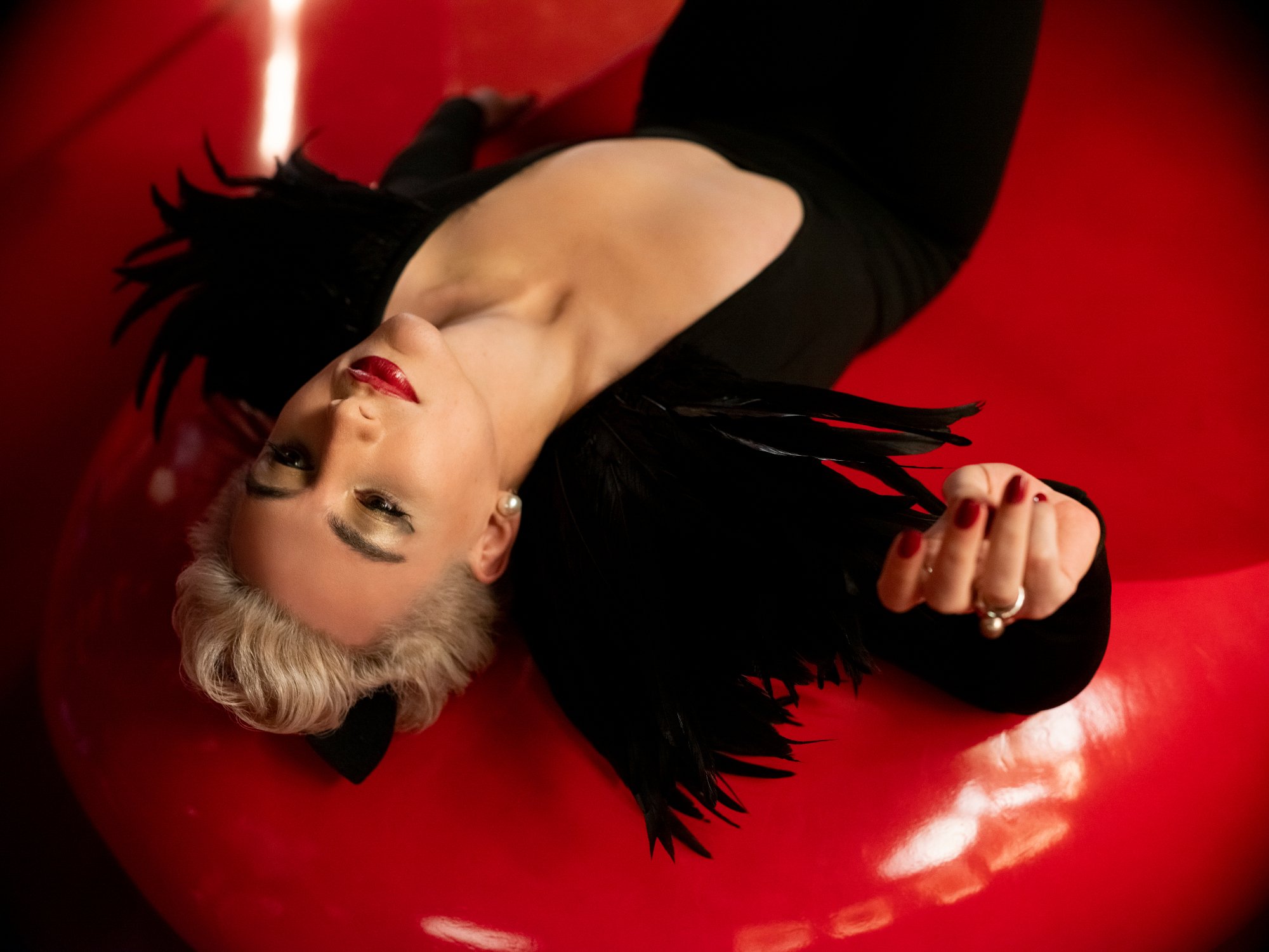 Mason Alexander Park as Desire in 'The Sandman' Season 1's ending episode. Desire is lying on a red seat and wearing red lipstick and a black outfit.