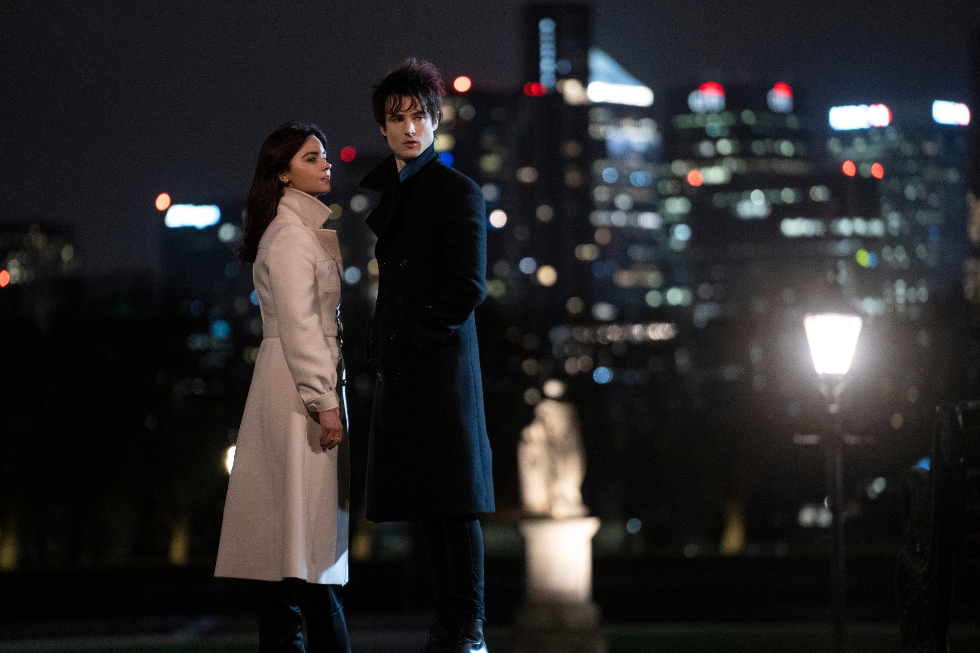 Jenna Coleman and Tom Sturridge in our article about 'The Sandman' Season 2. The pair is standing next to one another, and the city is behind them.