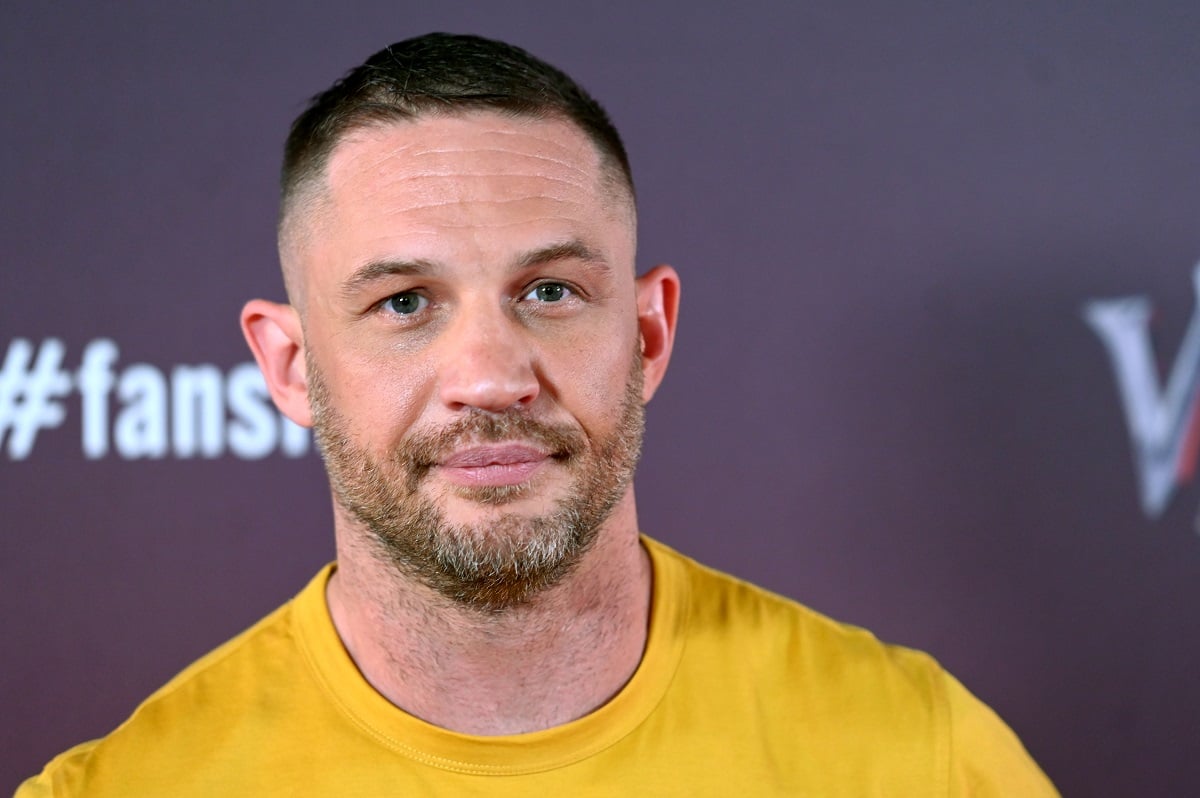 Tom Hardy smirking while wearing a yellow shirt.