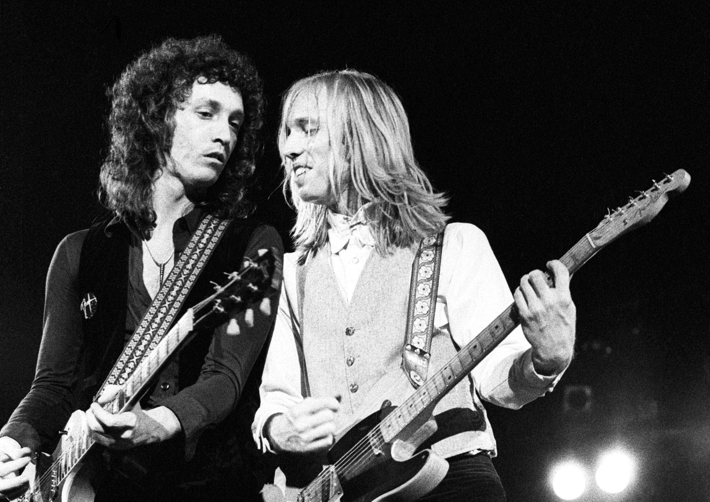 A black and white picture of bandmates Mike Campbell and Tom Petty playing guitar together.