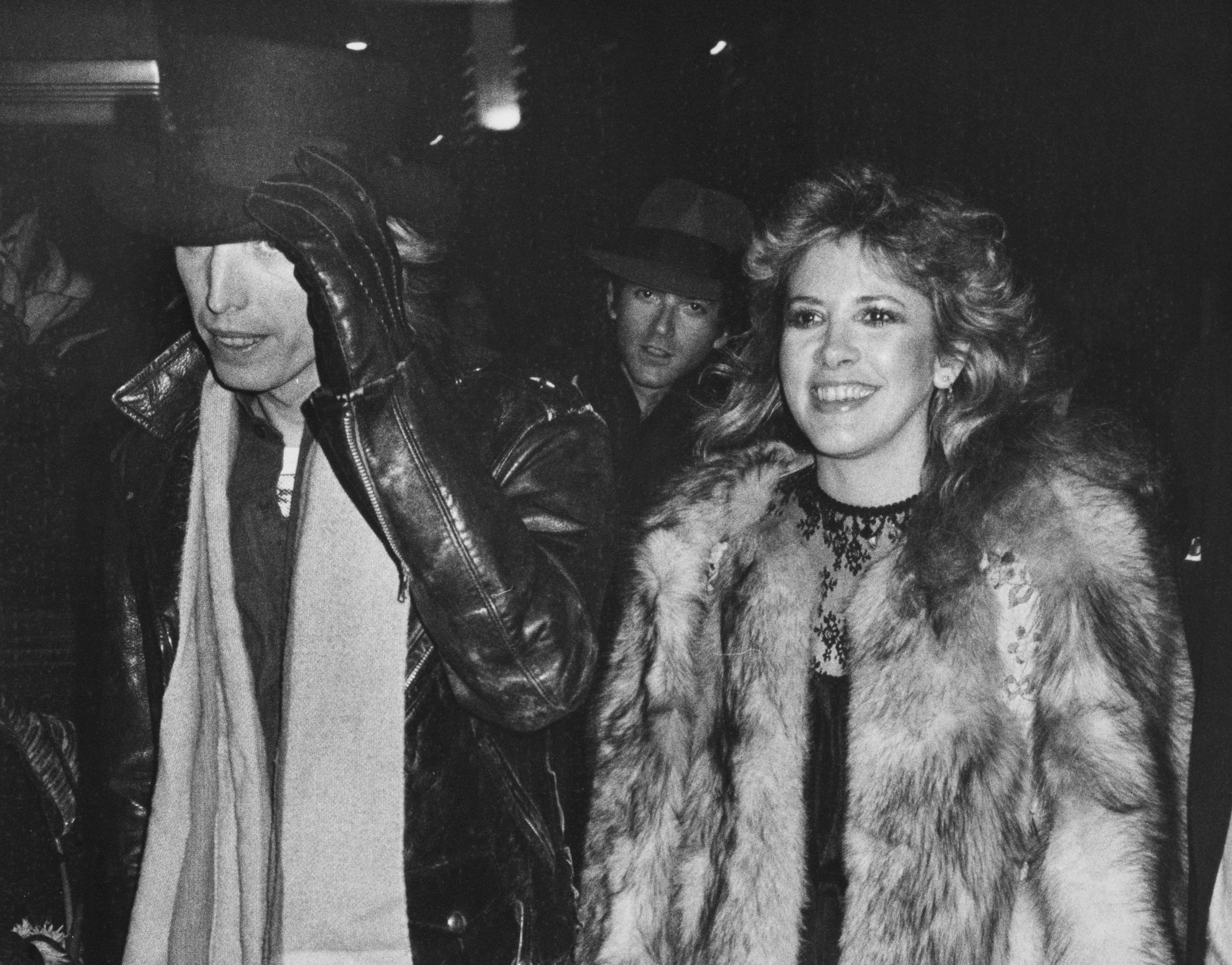 A black and white picture of Tom Petty and Stevie Nicks wearing coats and walking outside.