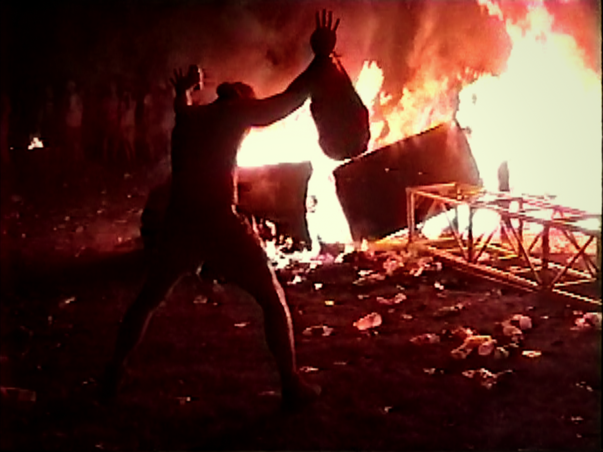 Production still from 'Trainwreck: Woodstock '99' featuring a person standing in front of a giant blaze.