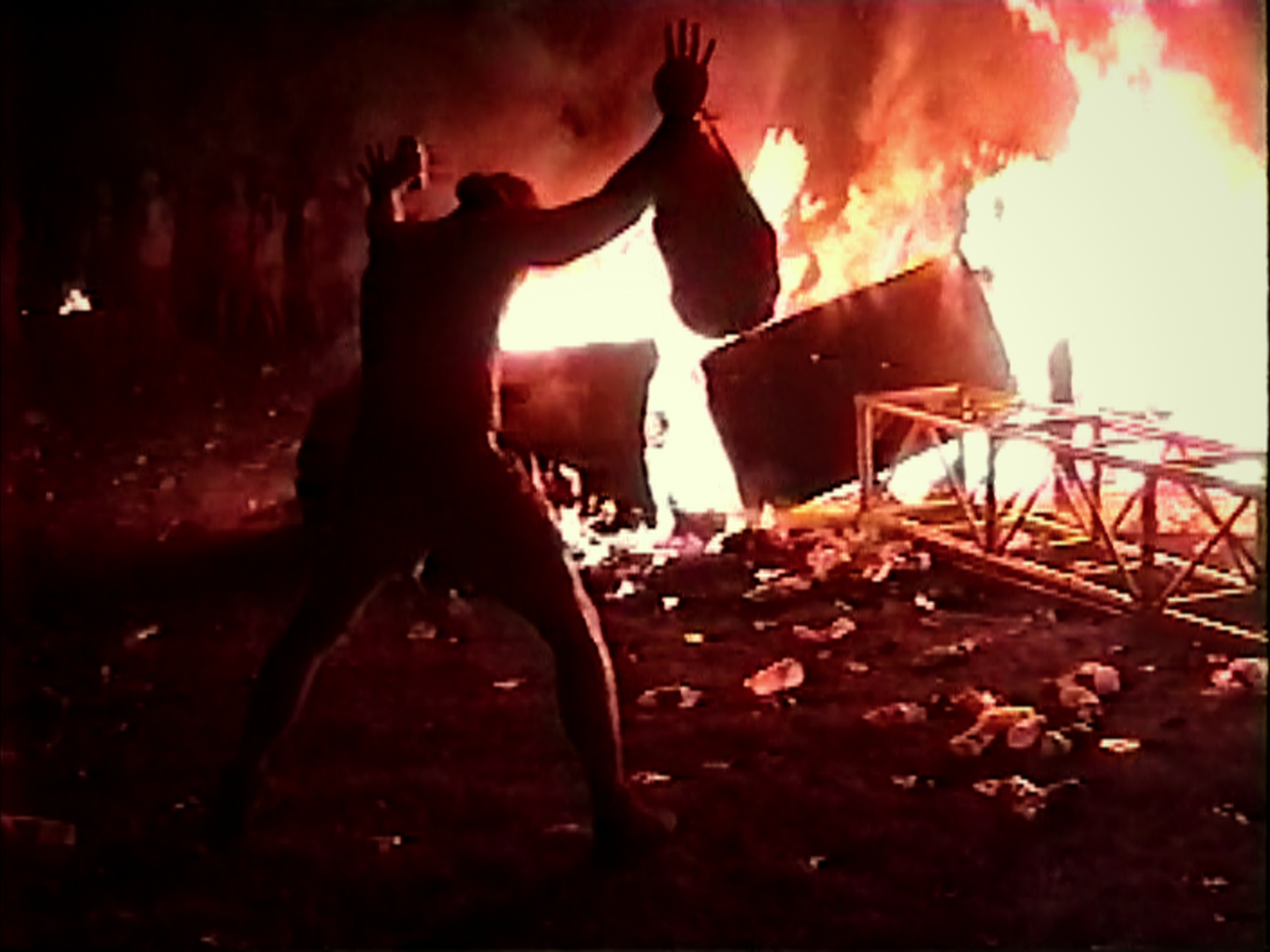 Production still of 'Trainwreck: Woodstock '99' with a person standing in front of a giant fire.