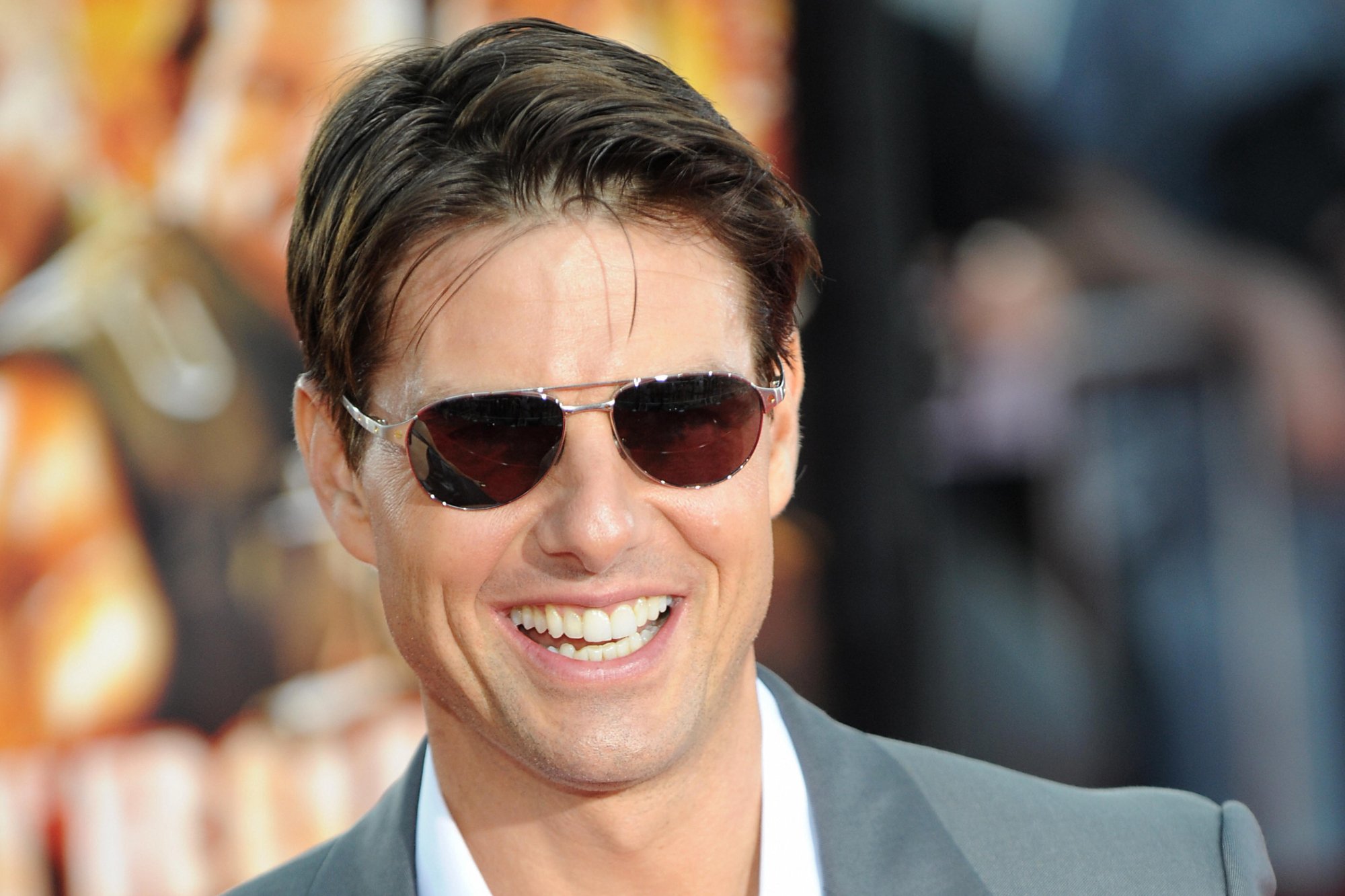 'Tropic Thunder' actor Tom Cruise, who played Les Grossman. He's smiling, wearing aviator sunglasses, and a grey suit in front of the movie poster.