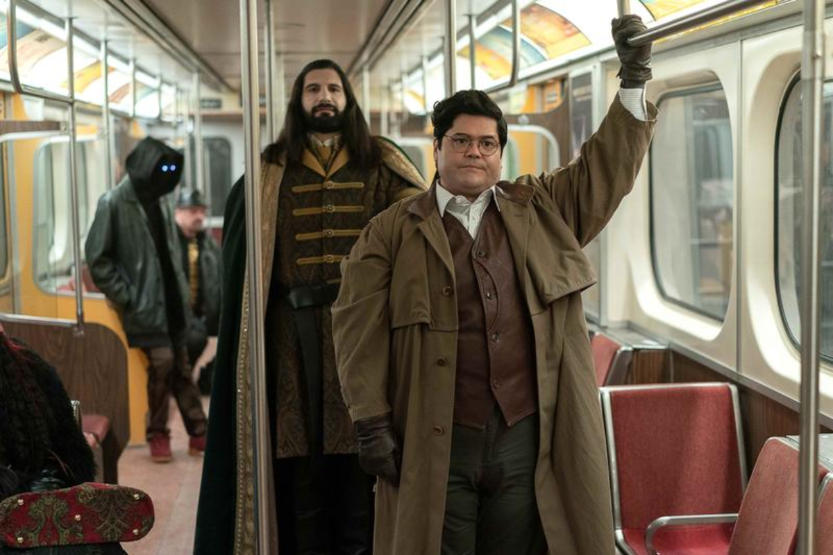 Kayvan Novak as Nandor and Harvey Guillén as Guillermo in What We Do in the Shadows. Nandor and Guillermo stand on the bus. 