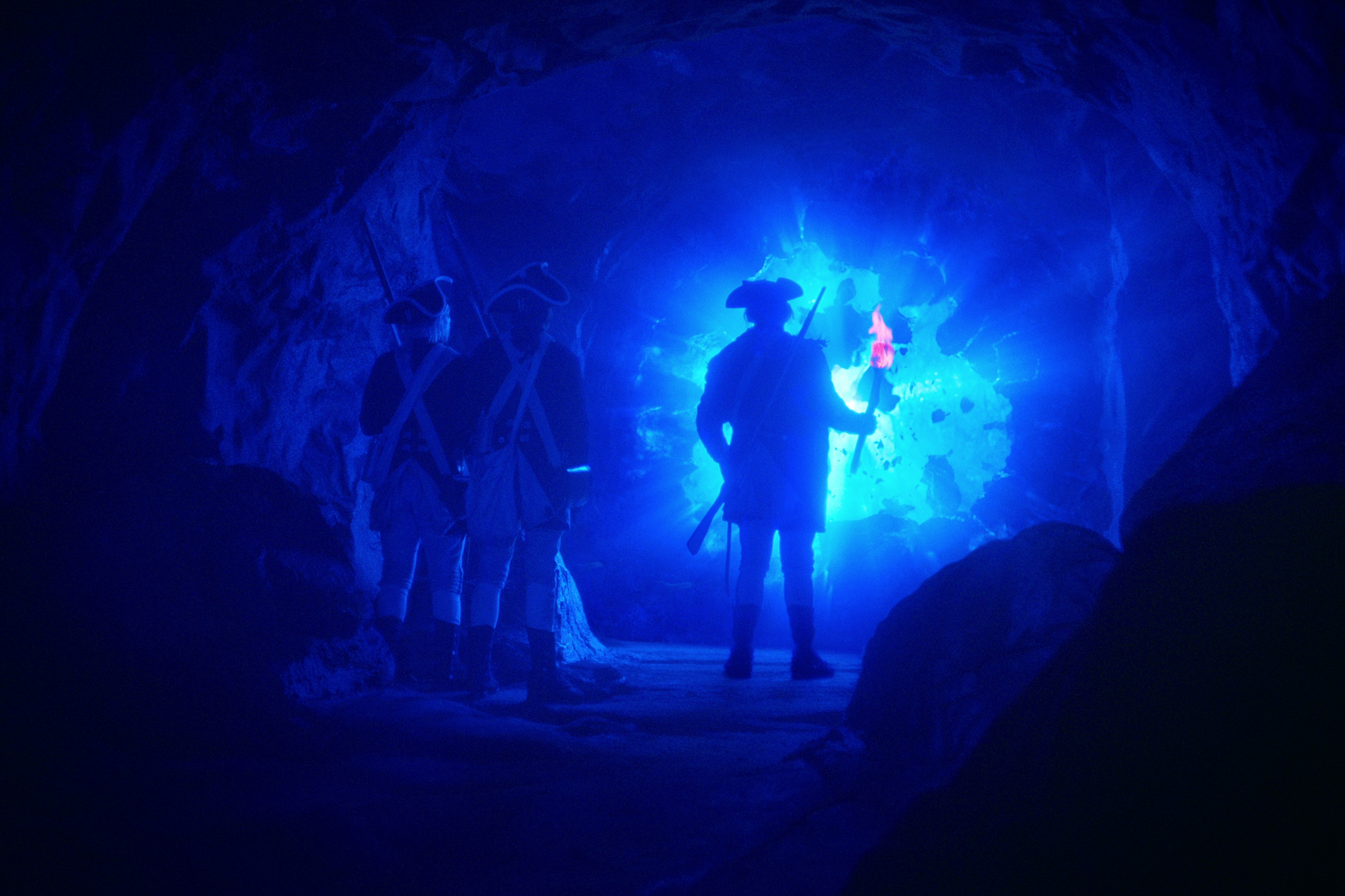 Ian Lake as Bolton, Jeff Lillico as Coffey, and Kevin Durand as Gideon in 'Locke & Key' Season 3 for our article about who dies. They're standing in a cave with blue light pouring out of the gateway to their world.