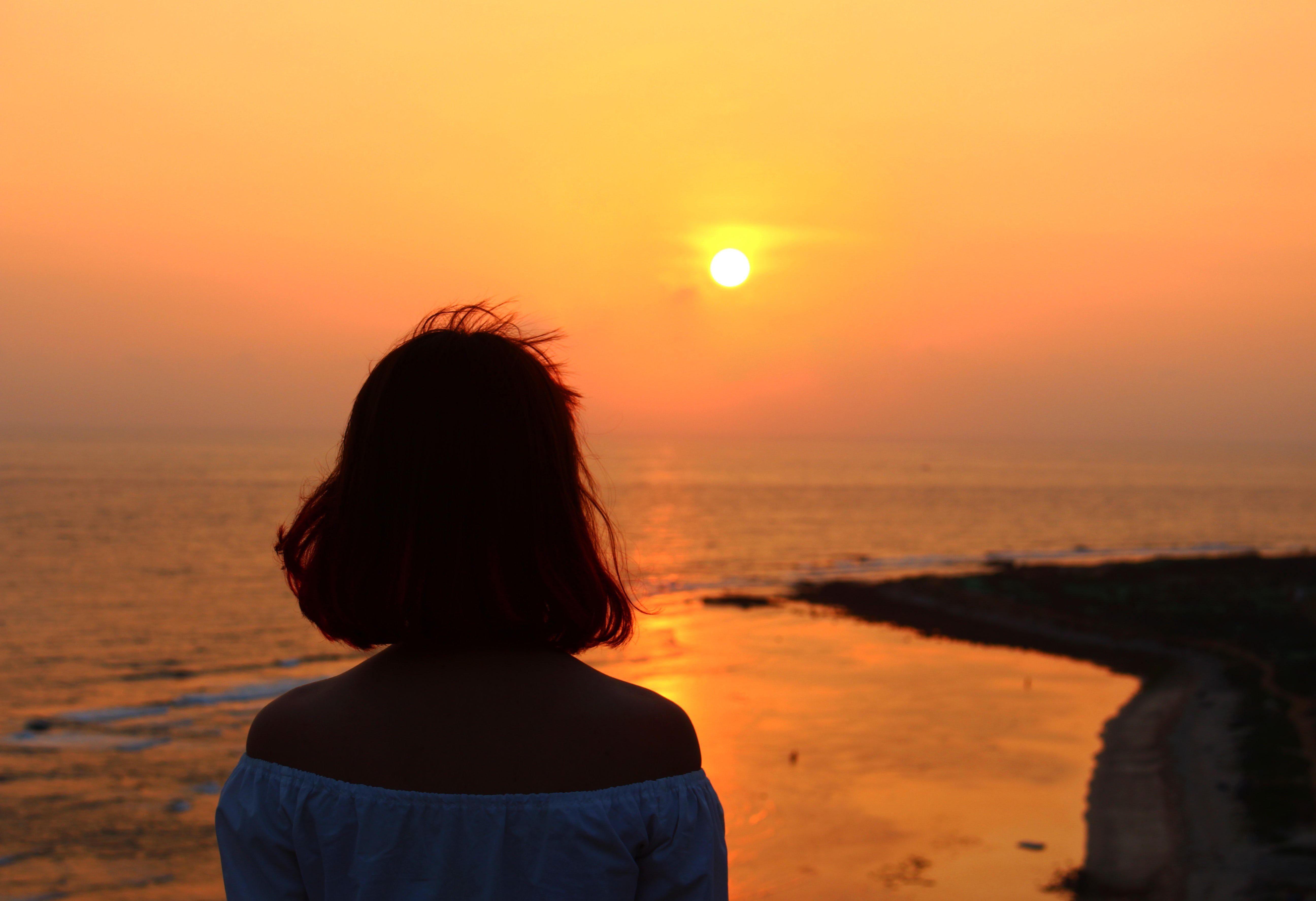 A woman looks at the sunset while walking on the beach.