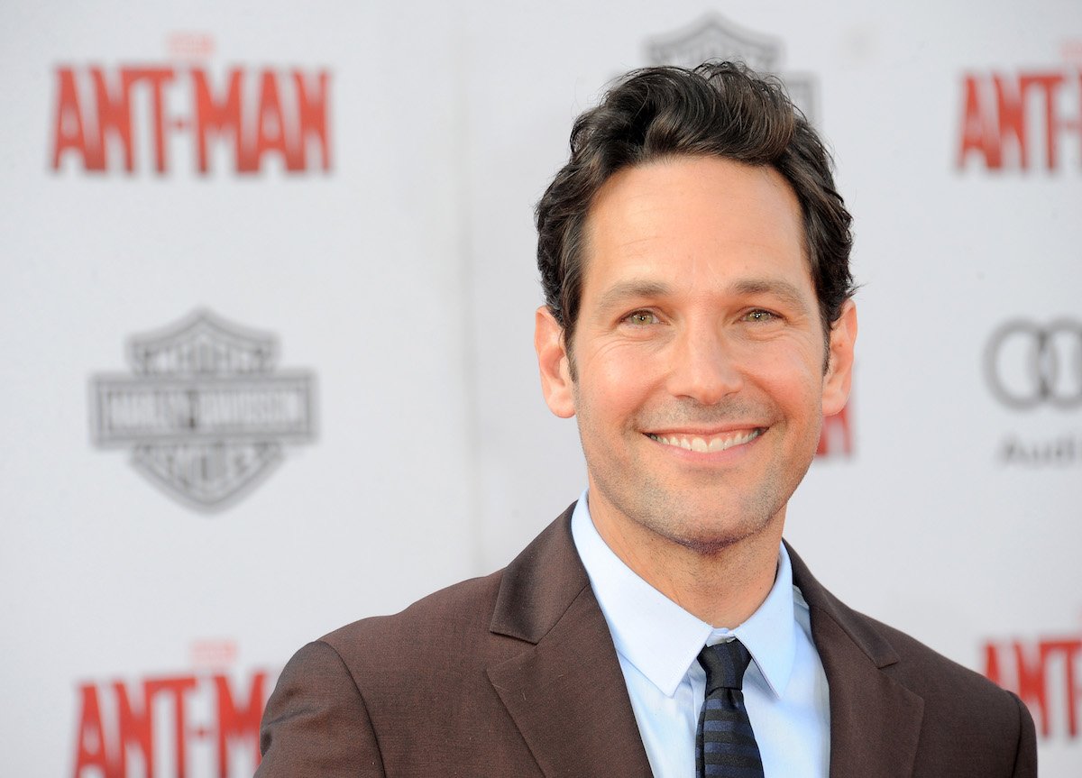 Paul Rudd smiling in front of an 'Ant-Man' backdrop, the first of the three Ant-Man movies