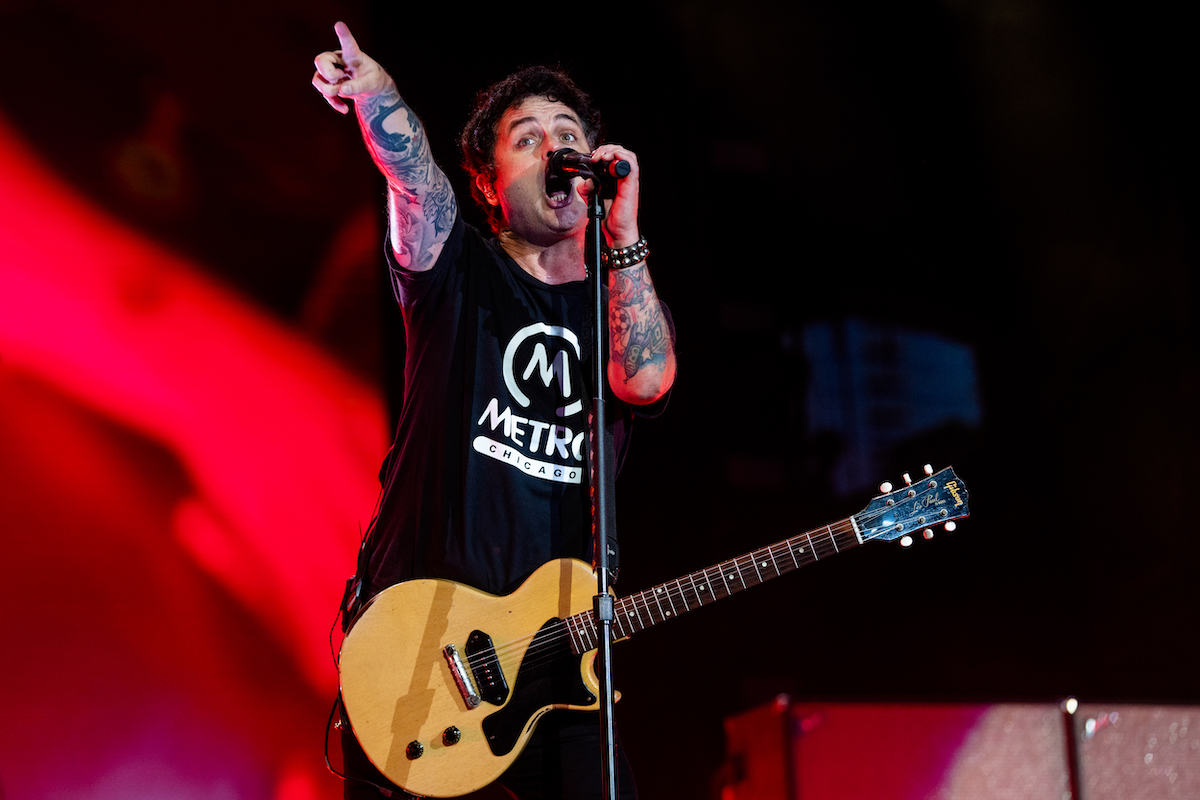 Green Day's Billie Joe Armstrong performs during Lollapalooza 2022, singing into a microphone and pointing to his right with a guitar around his neck.