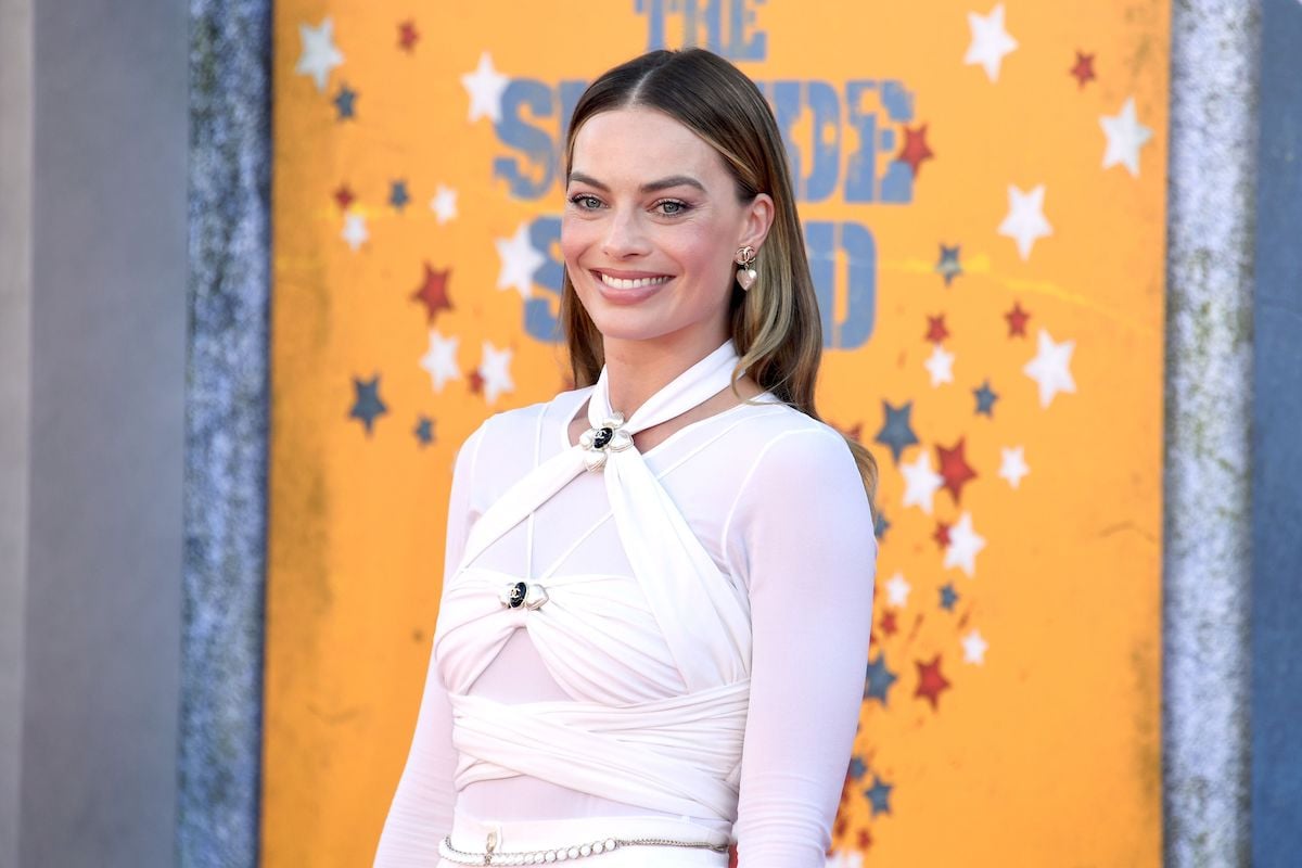 Margot Robbie in a white outfit posing in front of a 'The Suicide Squad' backdrop