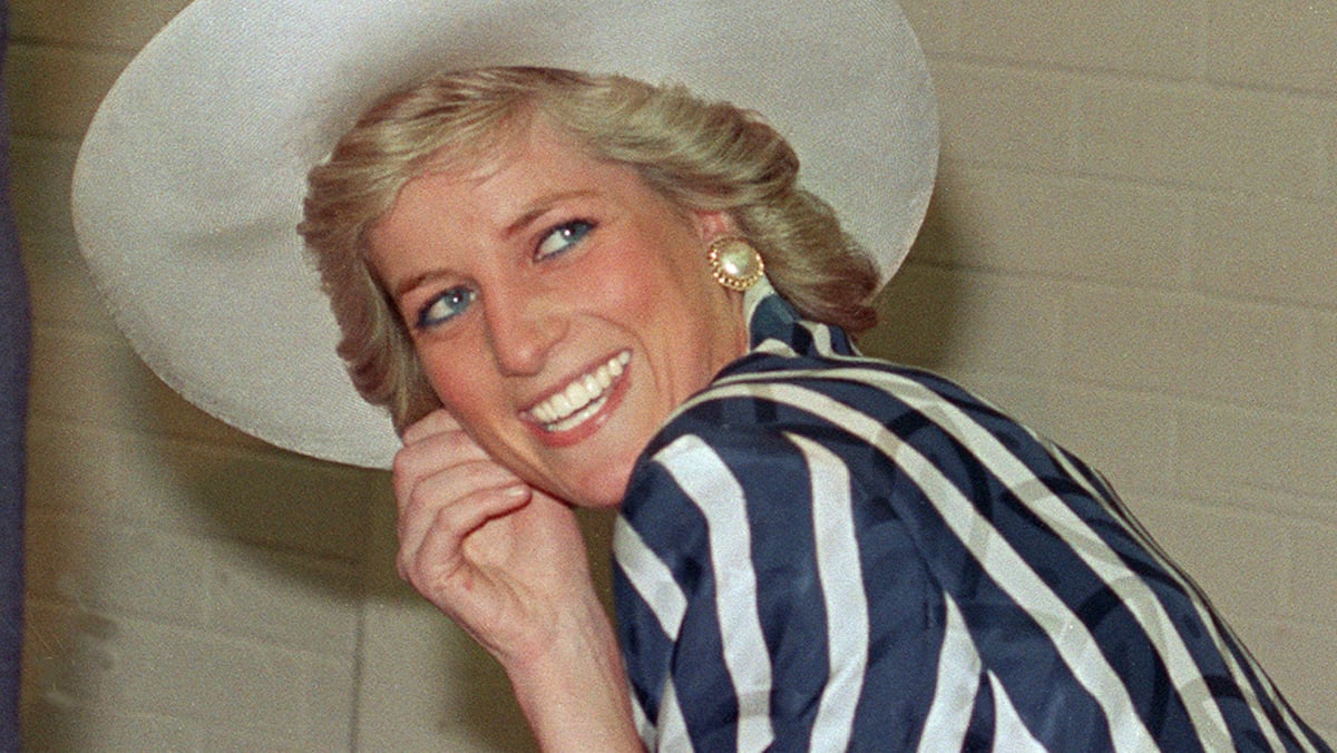 Princess Diana smiles wearing a striped dress and large white hat atop her head.