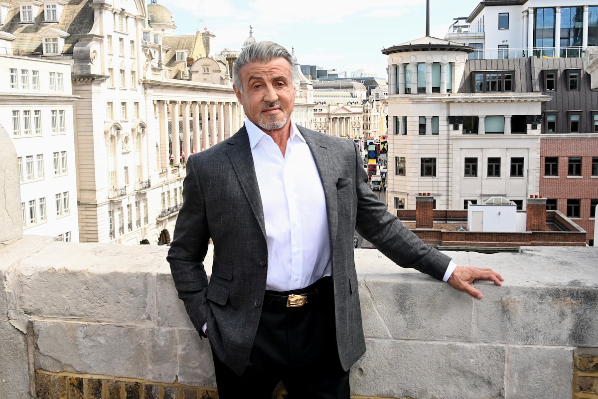 Sylvester Stallone of the 'Rocky' franchise that includes 'Creed' poses against a stone wall.