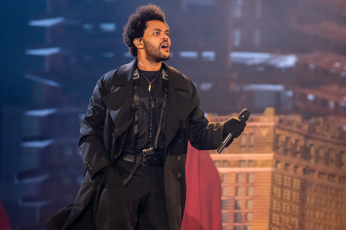 The Weeknd (Abel Makkonen Tesfaye) performs on stage in an all-black outfit holding a mic