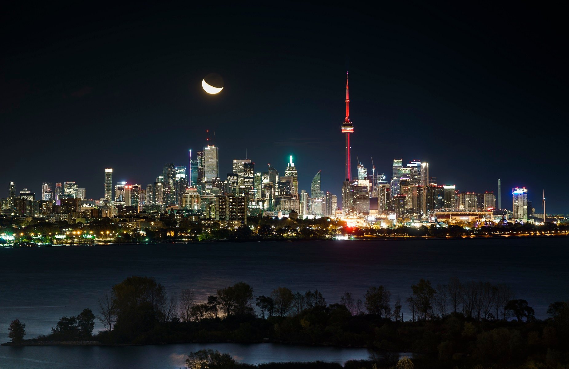 The moon rises behind the CN Tower and skyline in Toronto on October 23, 2019