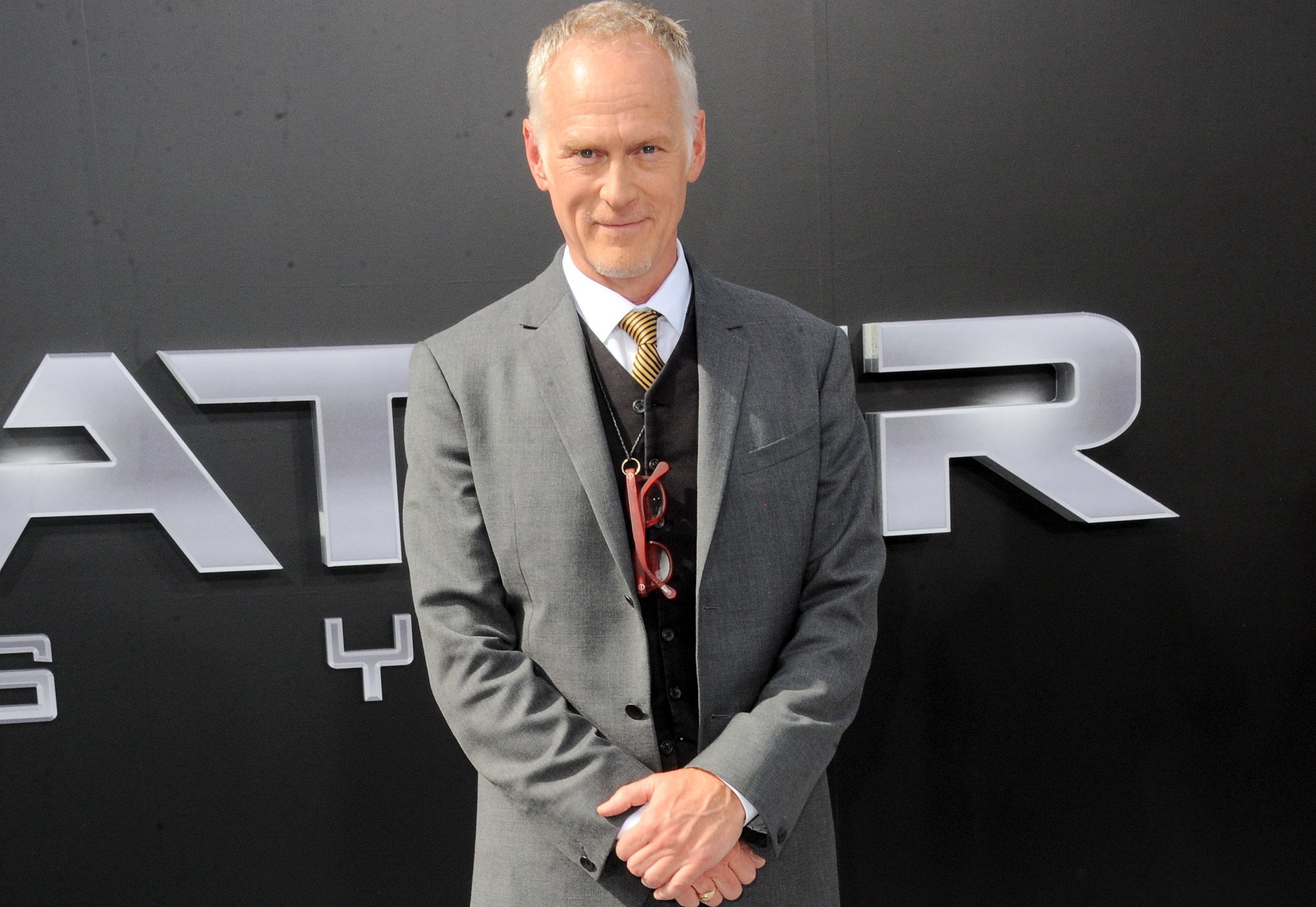 Director Alan Taylor, who is joining 'House of the Dragon' for season 2. He's wearing a white shirt, yellow tie, and gray suit in the photo. A pair of red glasses hangs around his neck.