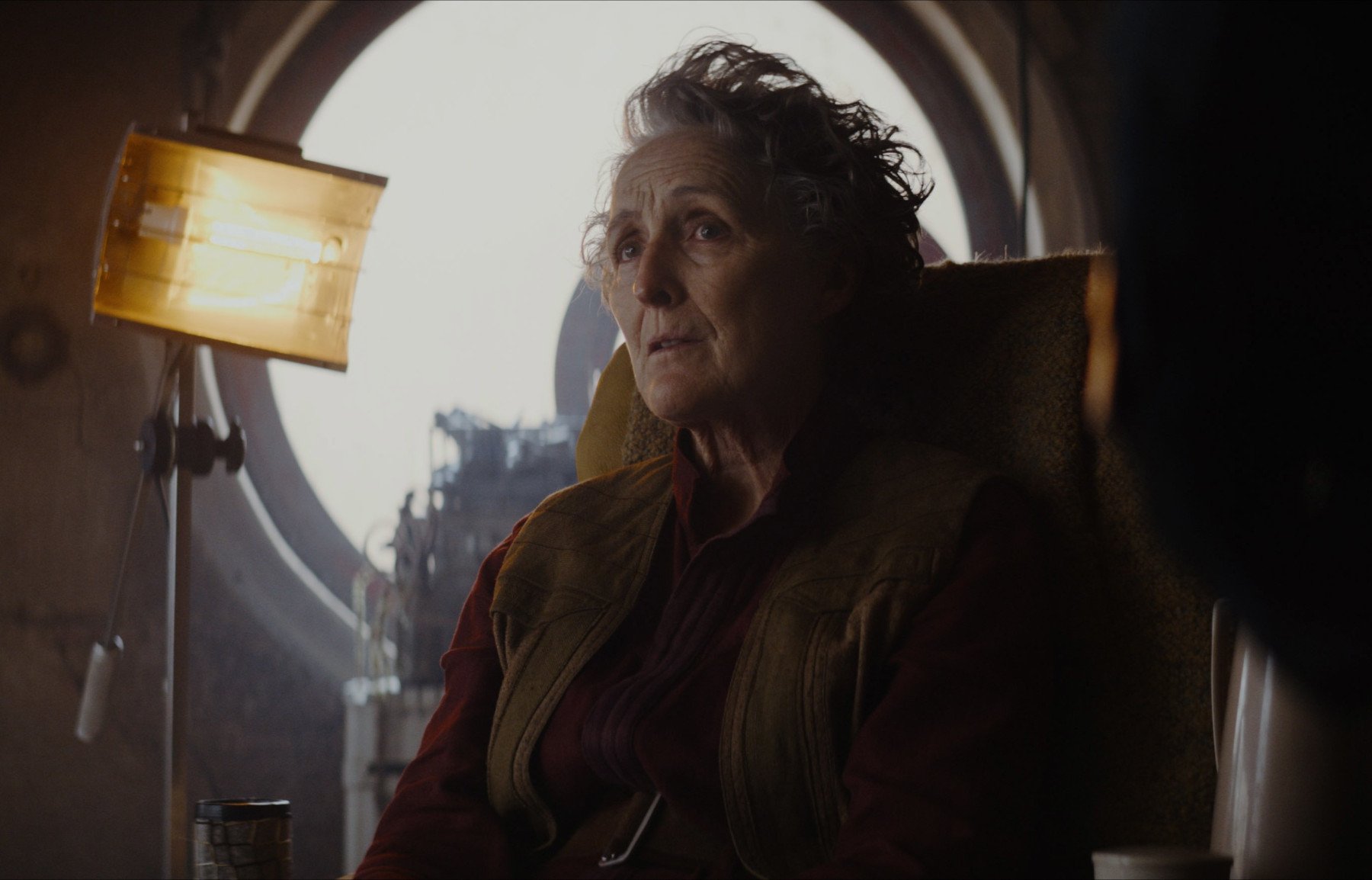 Fiona Shaw as Maarva during the ending of 'Andor' Episode 3. She's sitting in a chair, and there's a circular window behind her.