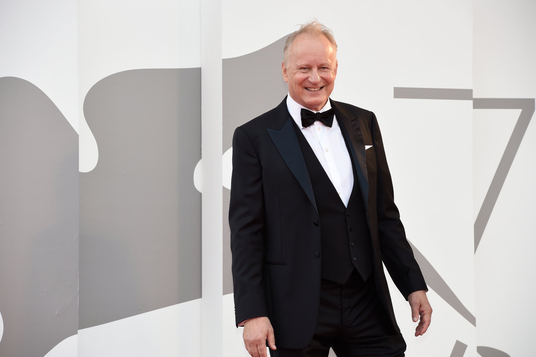 Actor Stellan Skarsgård who plays Luthen Rael in Andor. In the photo he is wearing a white shirt, black suit and black bow tie.
