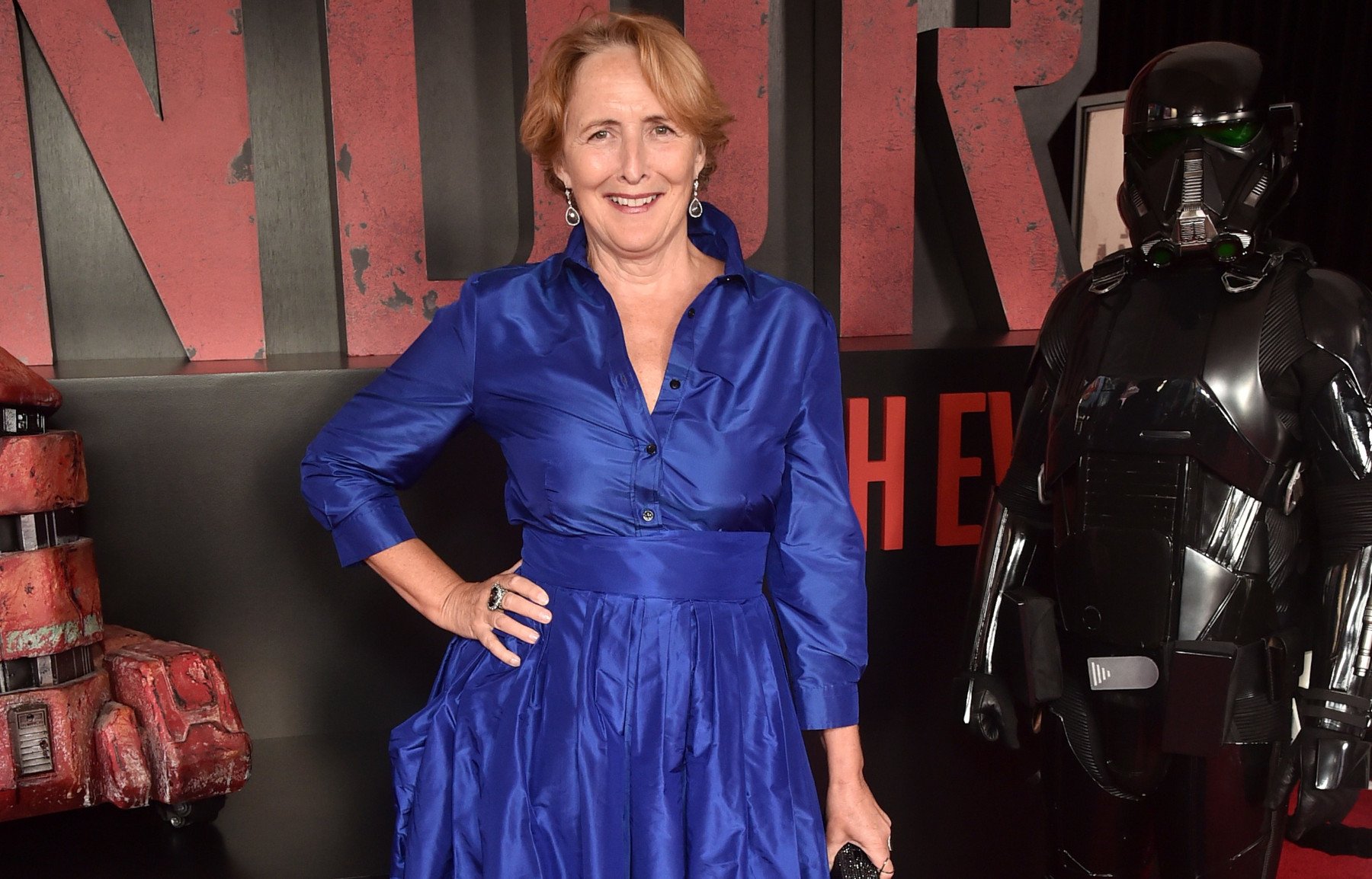 Actor Fiona Shaw, who plays Maarva in 'Andor.' She's wearing a blue, long-sleeved dress on the red carpet and standing next to a Stormtrooper statue and droid statue.