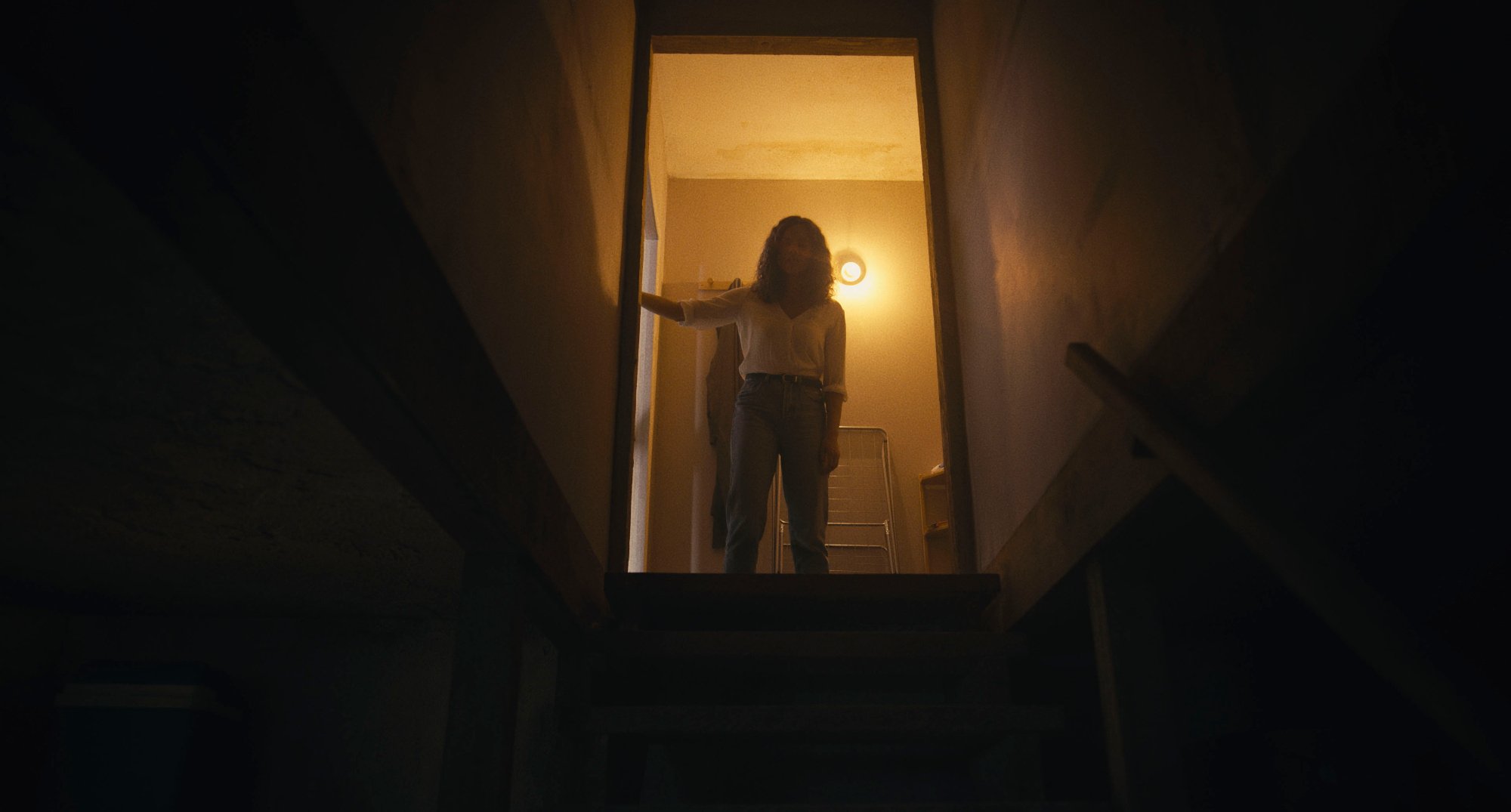 'Barbarian' Georgina Campbell as Tess standing in the doorway at the top of dark stairs down to the basement