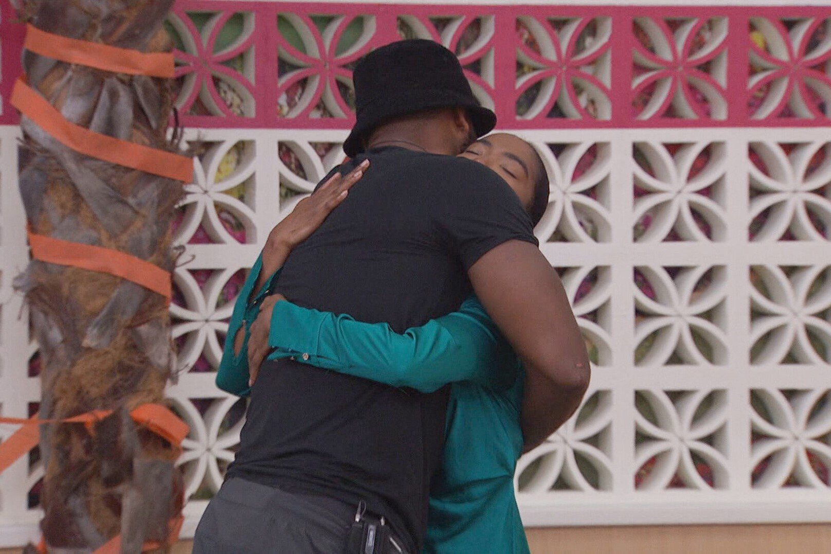 Monte Taylor and Taylor Hale, who star in 'Big Brother 24' on CBS, hug. Monte wears a black shirt, gray pants, and black bucket hat. Taylor wears a teal dress.