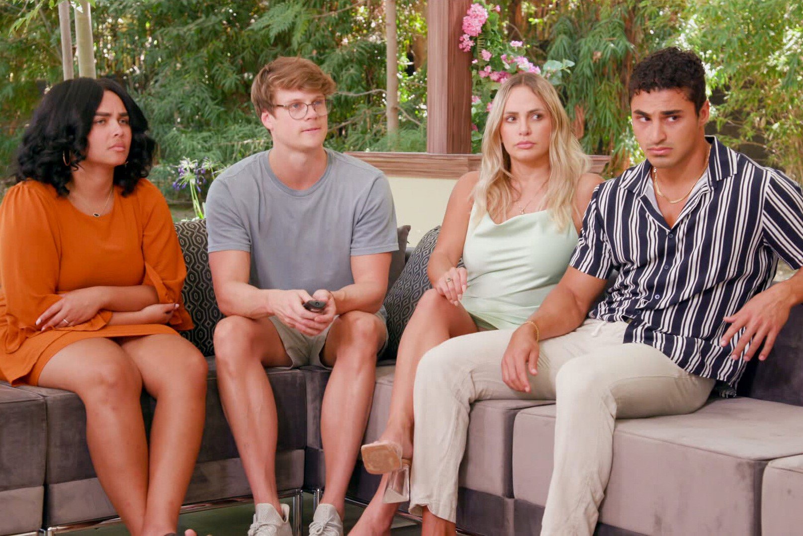 Jasmine Davis, Kyle Capener, Indy Santos, and Joseph Abdin, who are a part of the 'Big Brother 24' jury, sit on a couch. Jasmine wears an orange dress. Kyle wears a gray shirt and tan shorts. Indy wears a light green dress. Joseph wears a black and white striped shirt and tan pants.