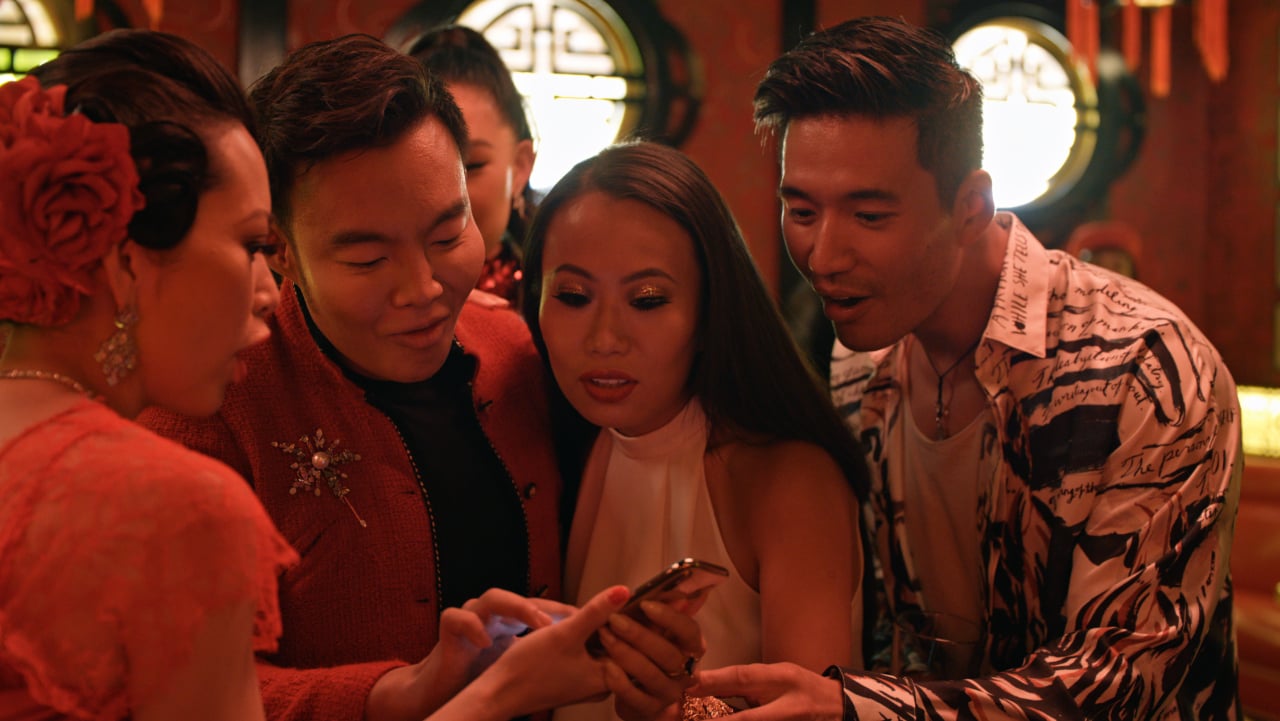 Christine Chiu, Kane Lim, Kelly Mi Li and Kevin Kreider standing next to each other looking at a phone during 'Bling Empire'