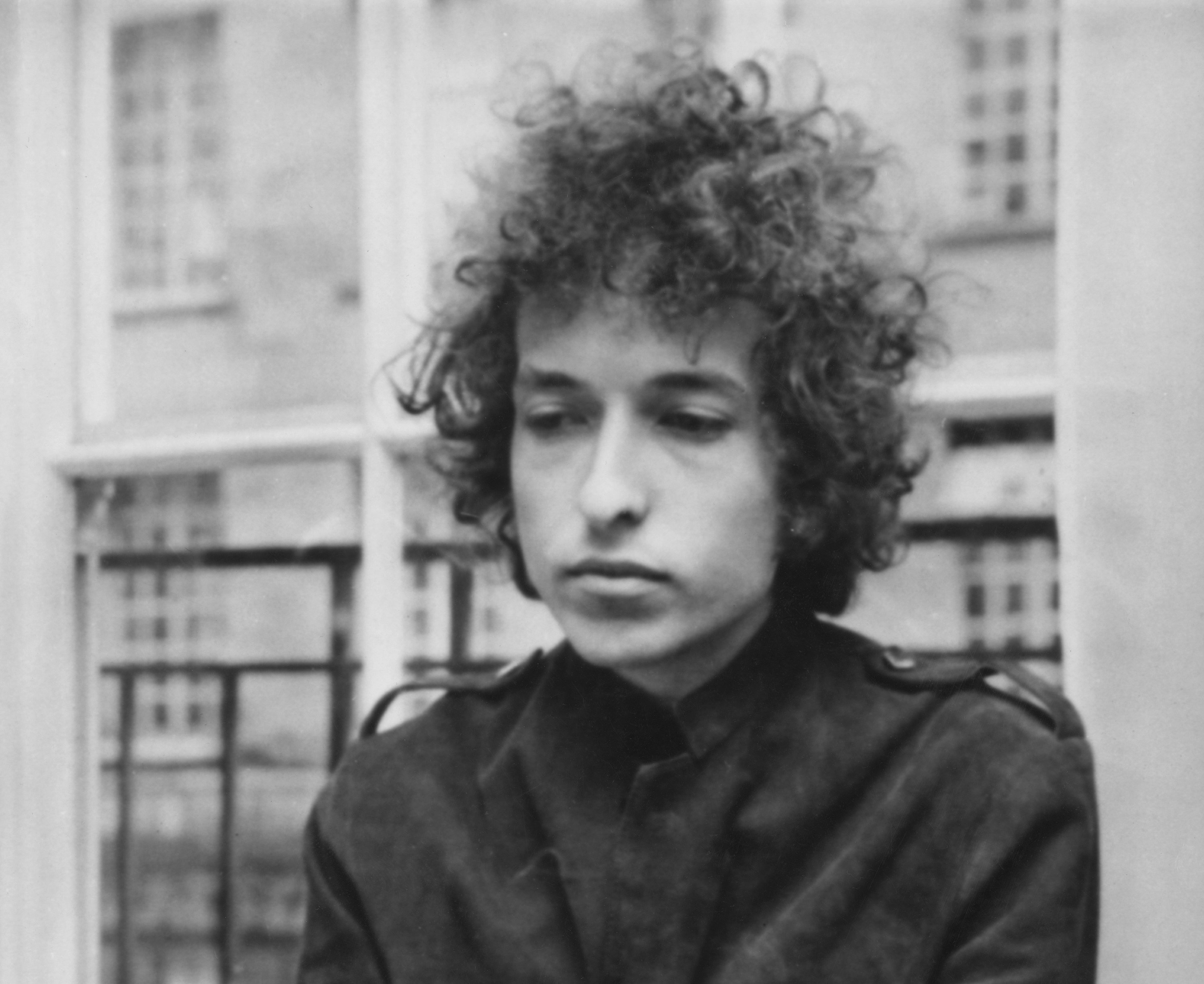 A black and white picture of Bob Dylan standing in front of a window. 