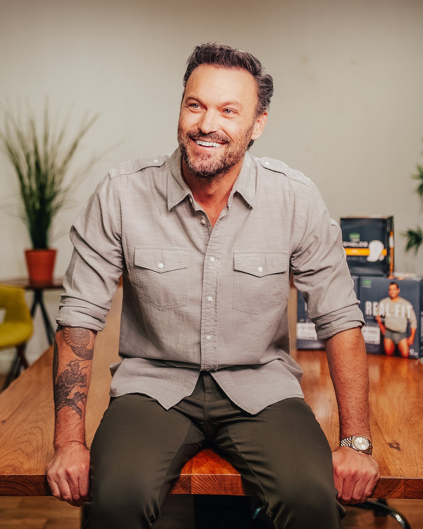 Brian Austin Green sits on the edge of a table and smiles