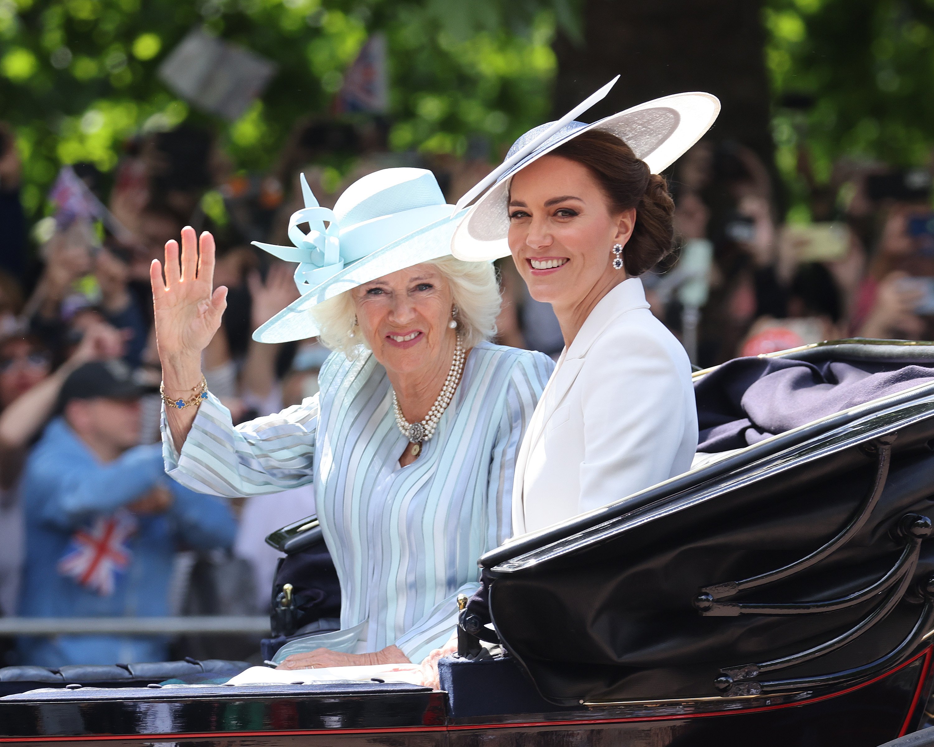 Camilla Parker Bowles waving and Kate Middleton smiling as they ride in a carriage during Trooping The Colour