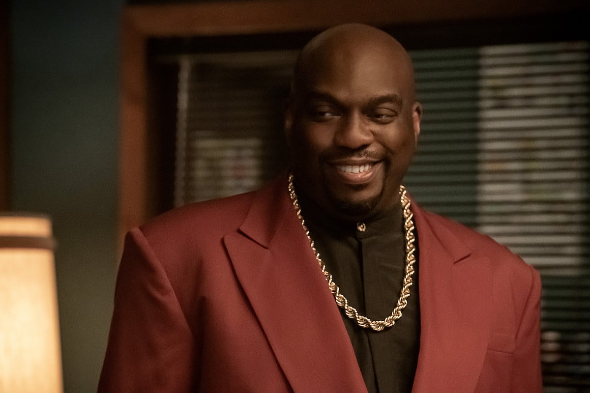 Omar J. Dorsey as Cartier Cartier “Duns” Fareed smiling while wearing a red blazer and gold chainin 'Power Book III: Raising Kanan'