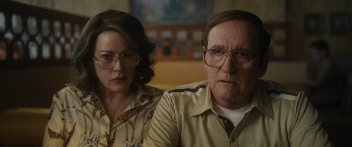 Molly Ringwald as Shari and Richard Jenkins as Lionel in DAHMER —Monster: The Jeffrey Dahmer Story. Shari and Lionel wear large glasses and sit on the couch.