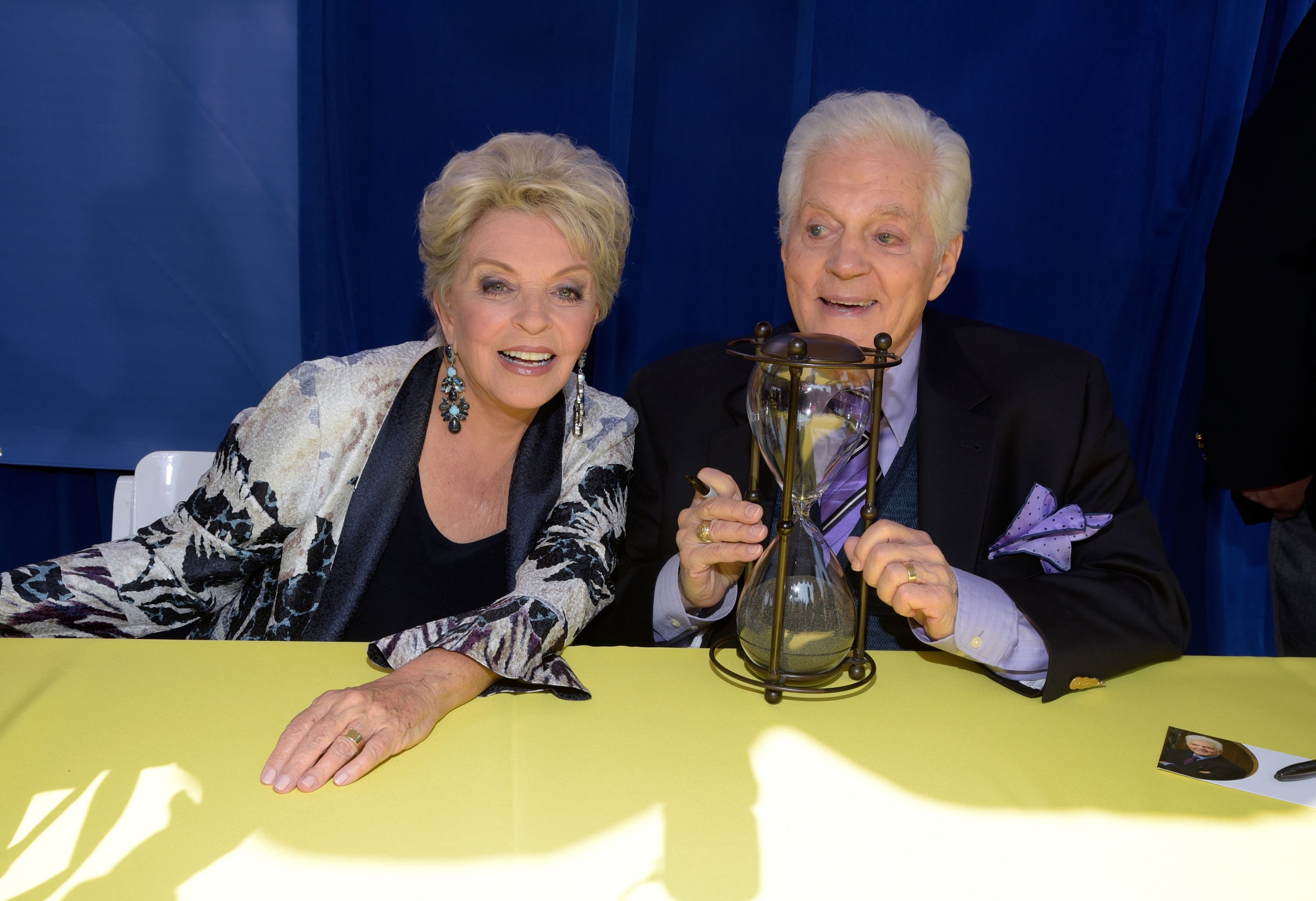 'Days of Our Lives' star Susan Hayes in a black and white blouse; and Bill Hayes in a blue suit pose with an hourglass.