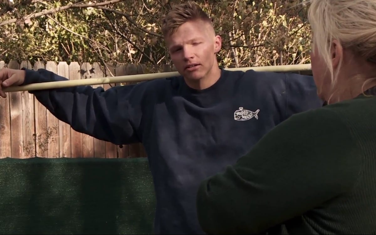 Garrison Brown standing outside with a rake on his shoulders in ‘Sister Wives’ Season 16 on TLC