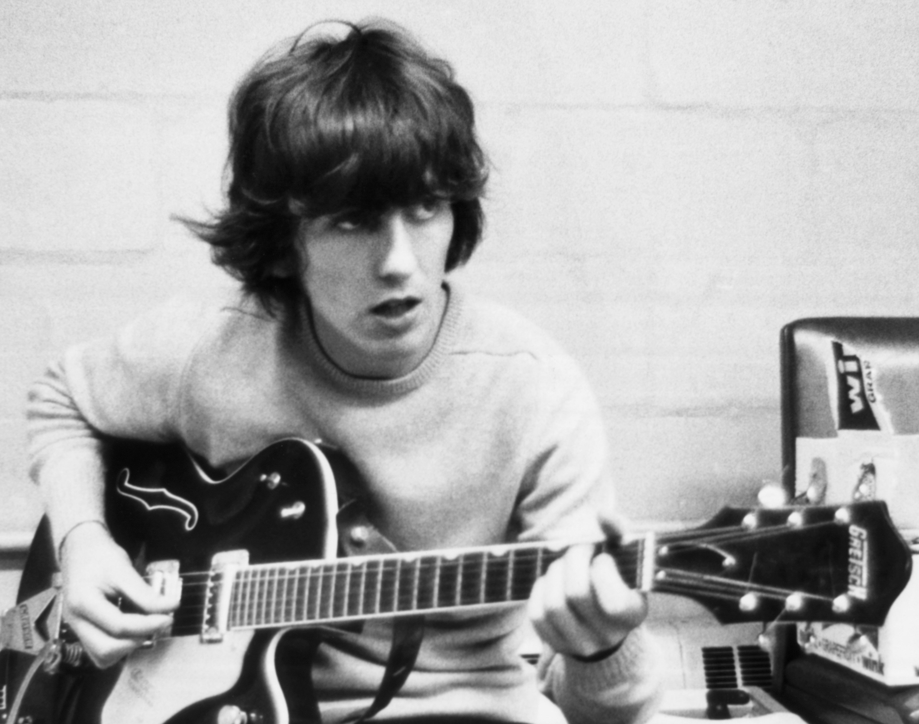 A black and white picture of George Harrison sitting and holding a guitar.