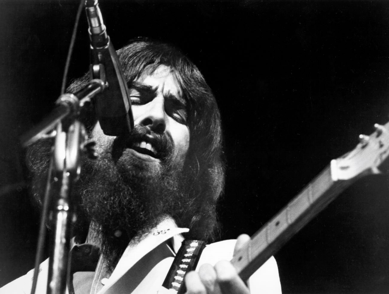 A black and white picture of George Harrison singing into a microphone and playing guitar.
