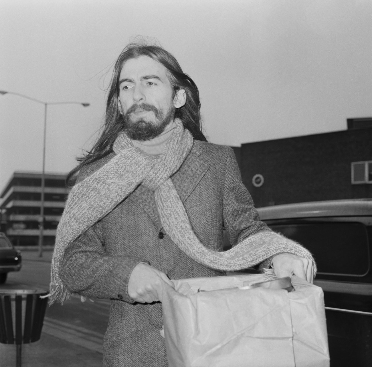 A black and white picture of George Harrison wearing a scarf and holding a box.